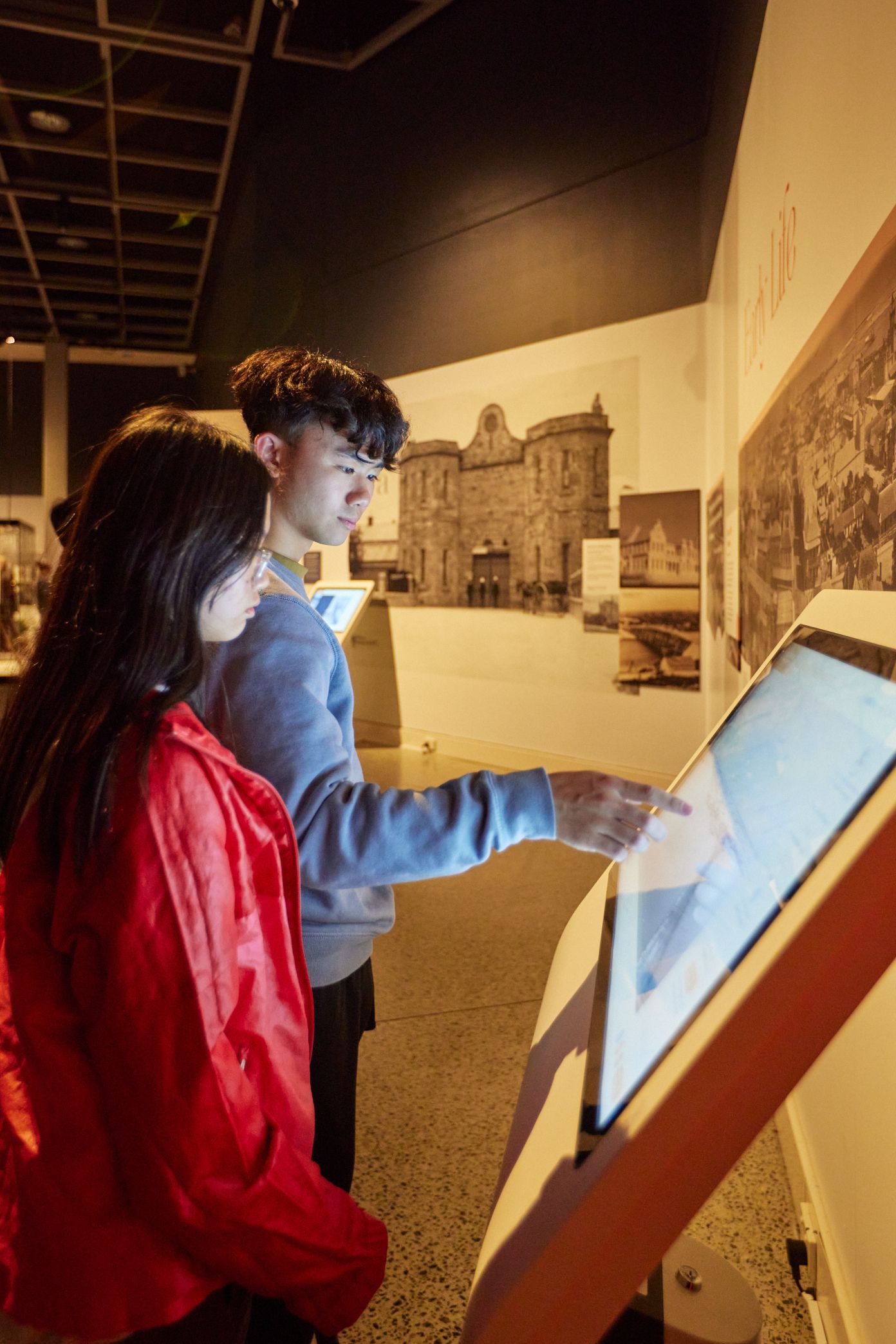 Two young people using a touch screen inside an exhibition of sepia images