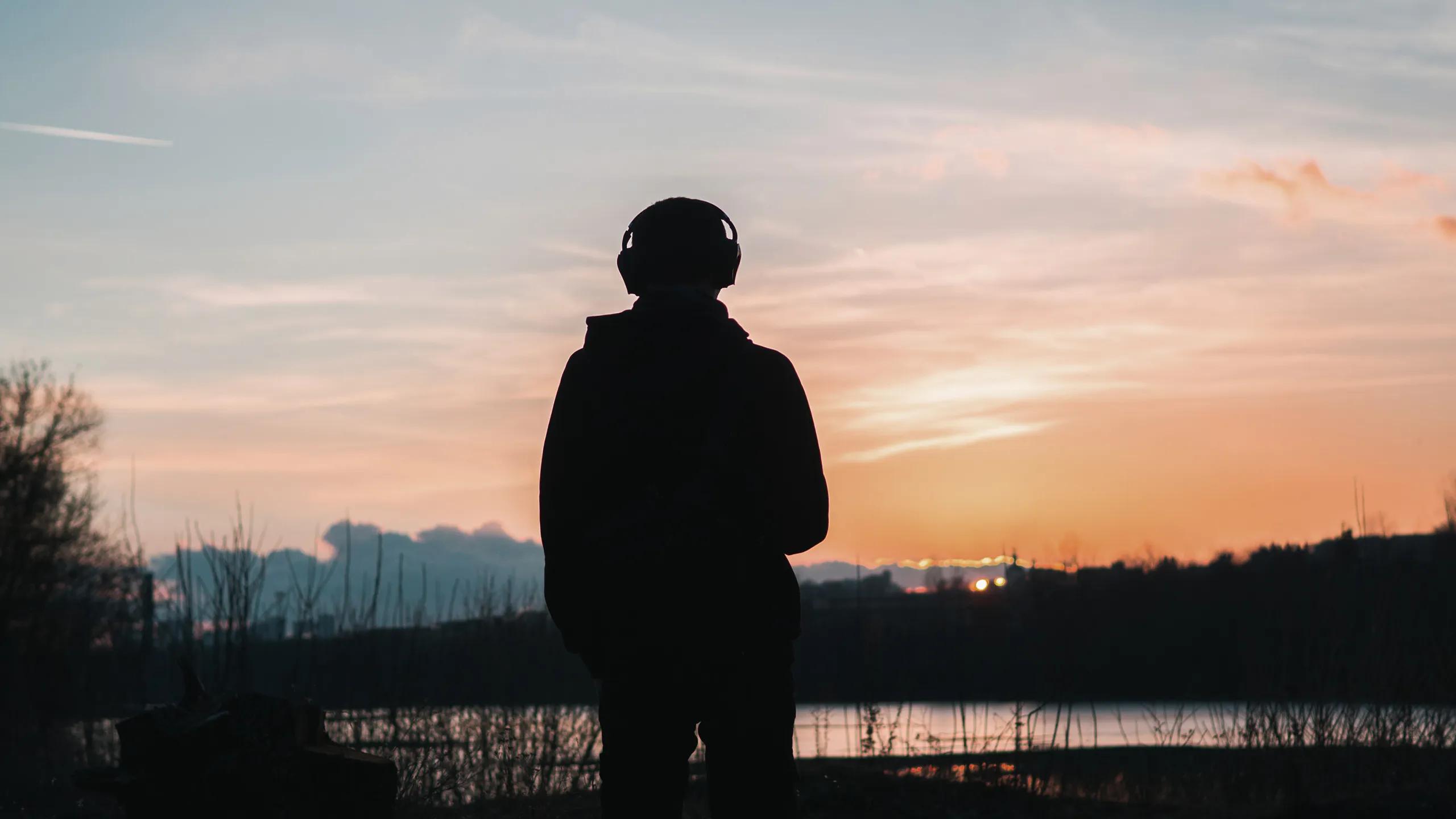 A photo of a silhouette of a man standing with some headphones on.