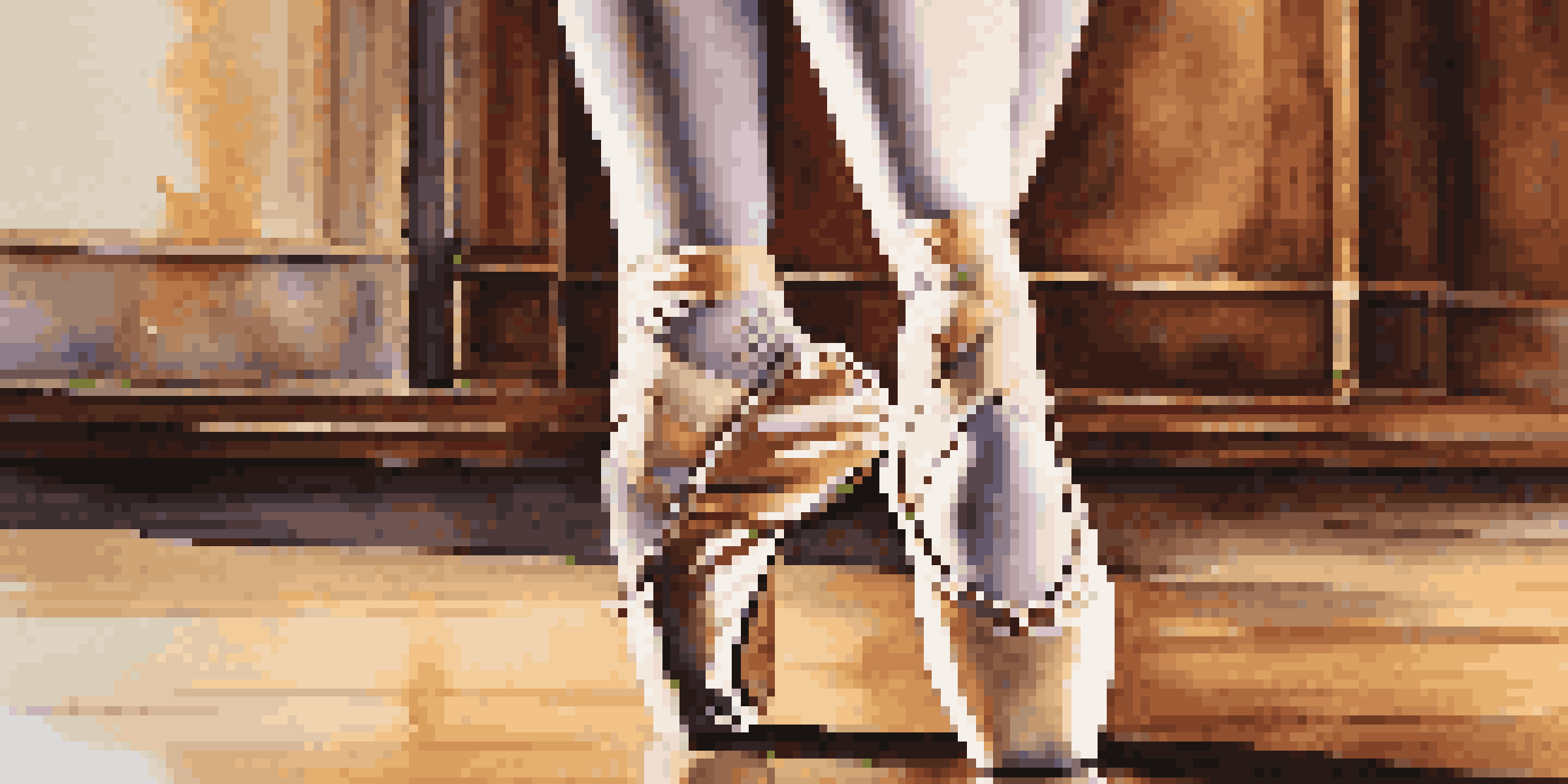 A close-up of a dancer's feet in ballet shoes on a wooden floor, with soft lighting accentuating the dancer's pose and a blurred theater stage in the background.