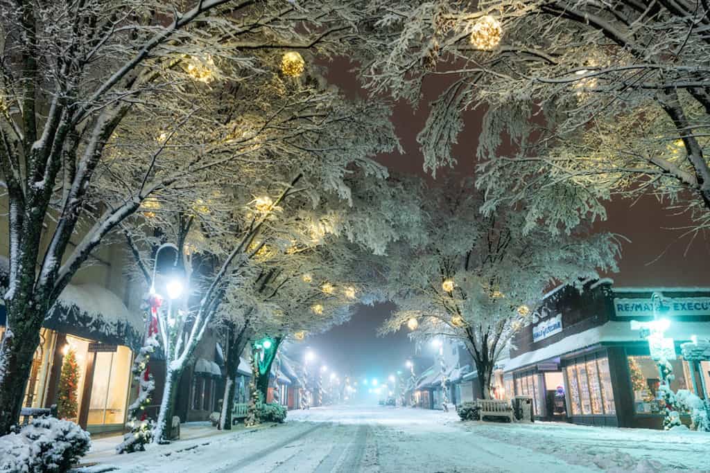 Snow-covered trees adorned with soft-glowing lanterns hang above the icy streets of Downtown Waynesville in the winter.
