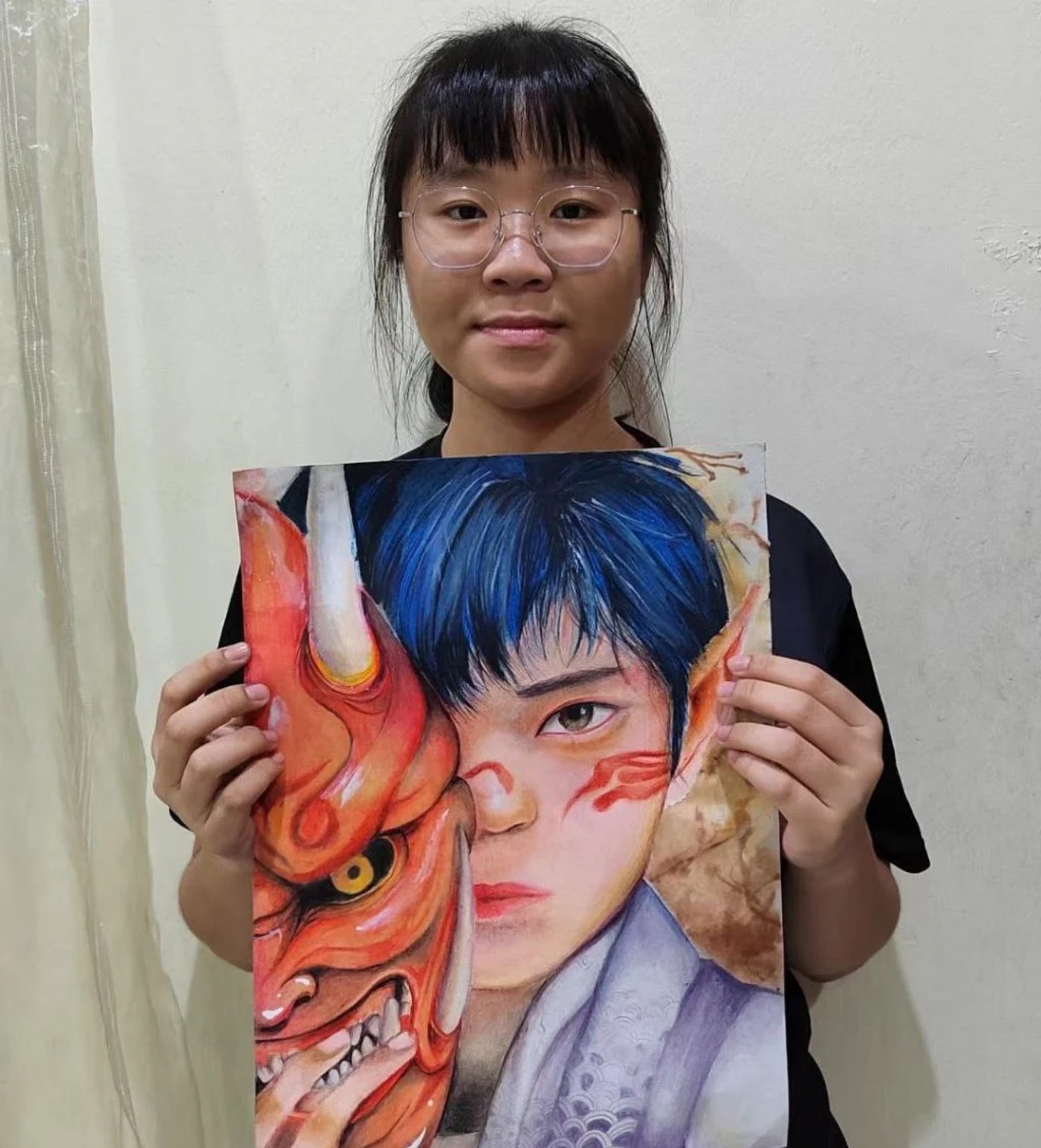 Student holding a blue-haired portrait beside a red mask