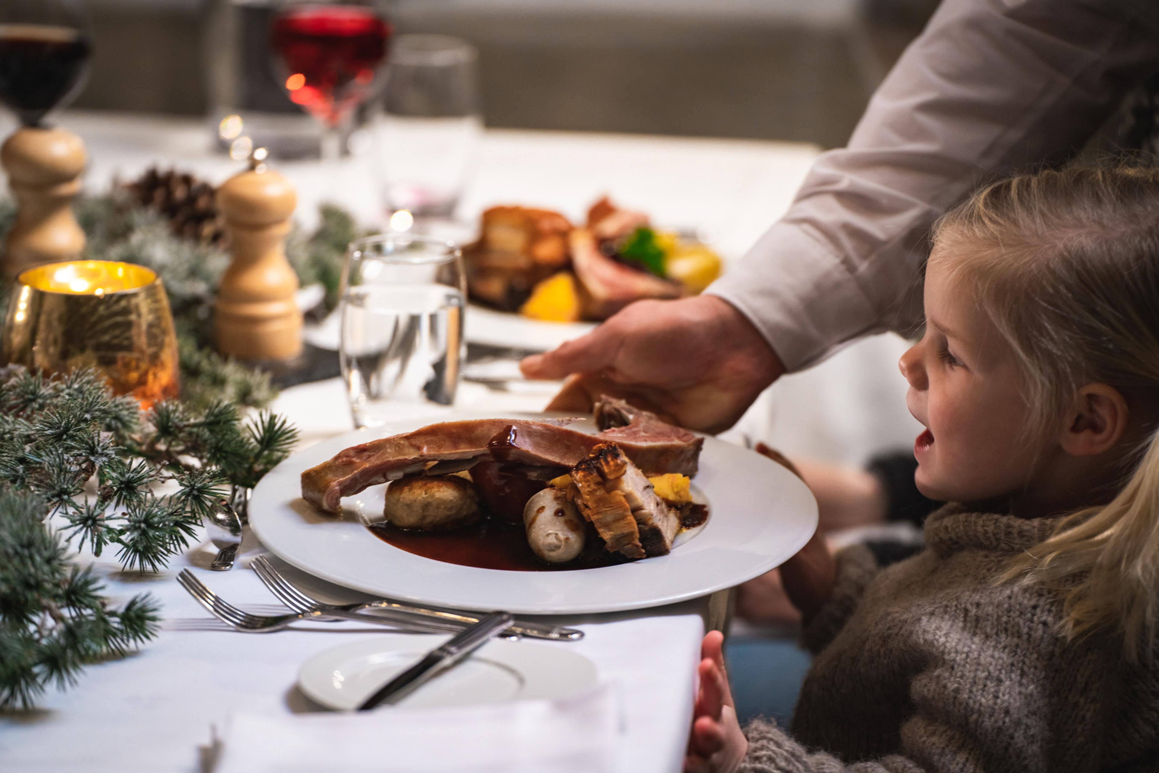 Et barn får servert en tallerken fylt med julemat ved et bord dekket av julepynt.