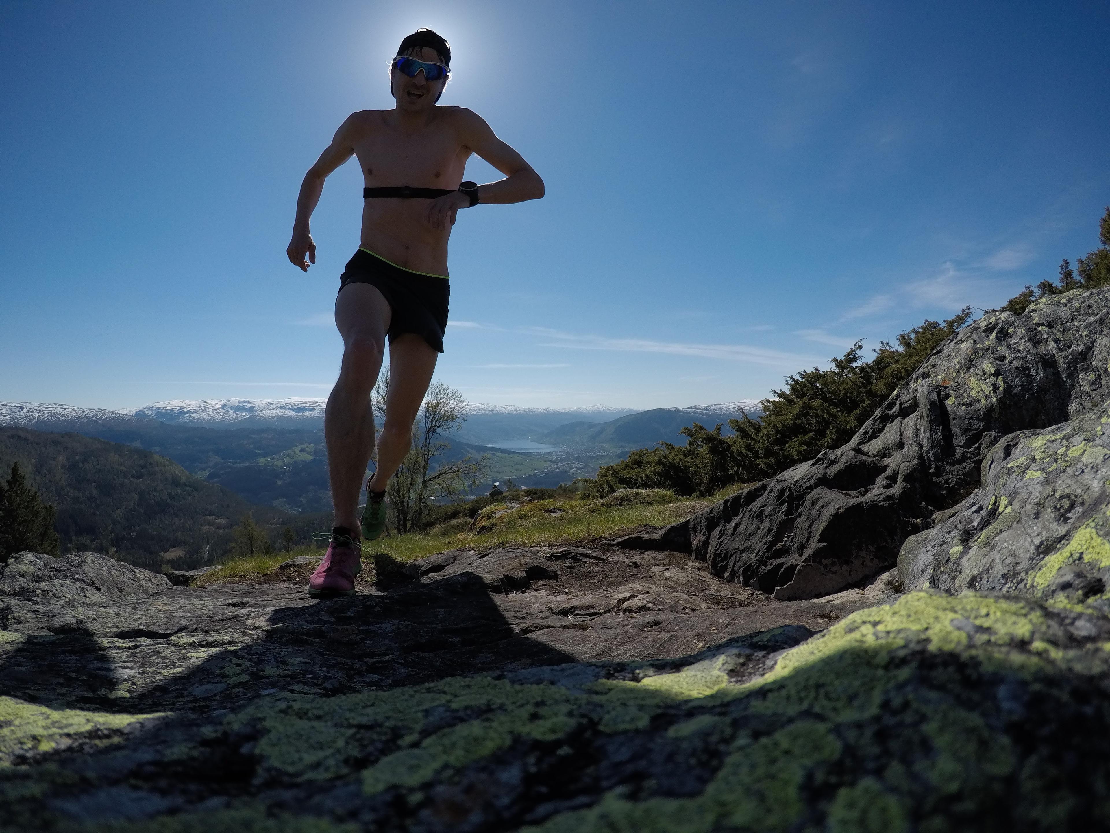 Mann springer på høgfjellet en sommerdag med utsikt over snødekte fjelltopper.