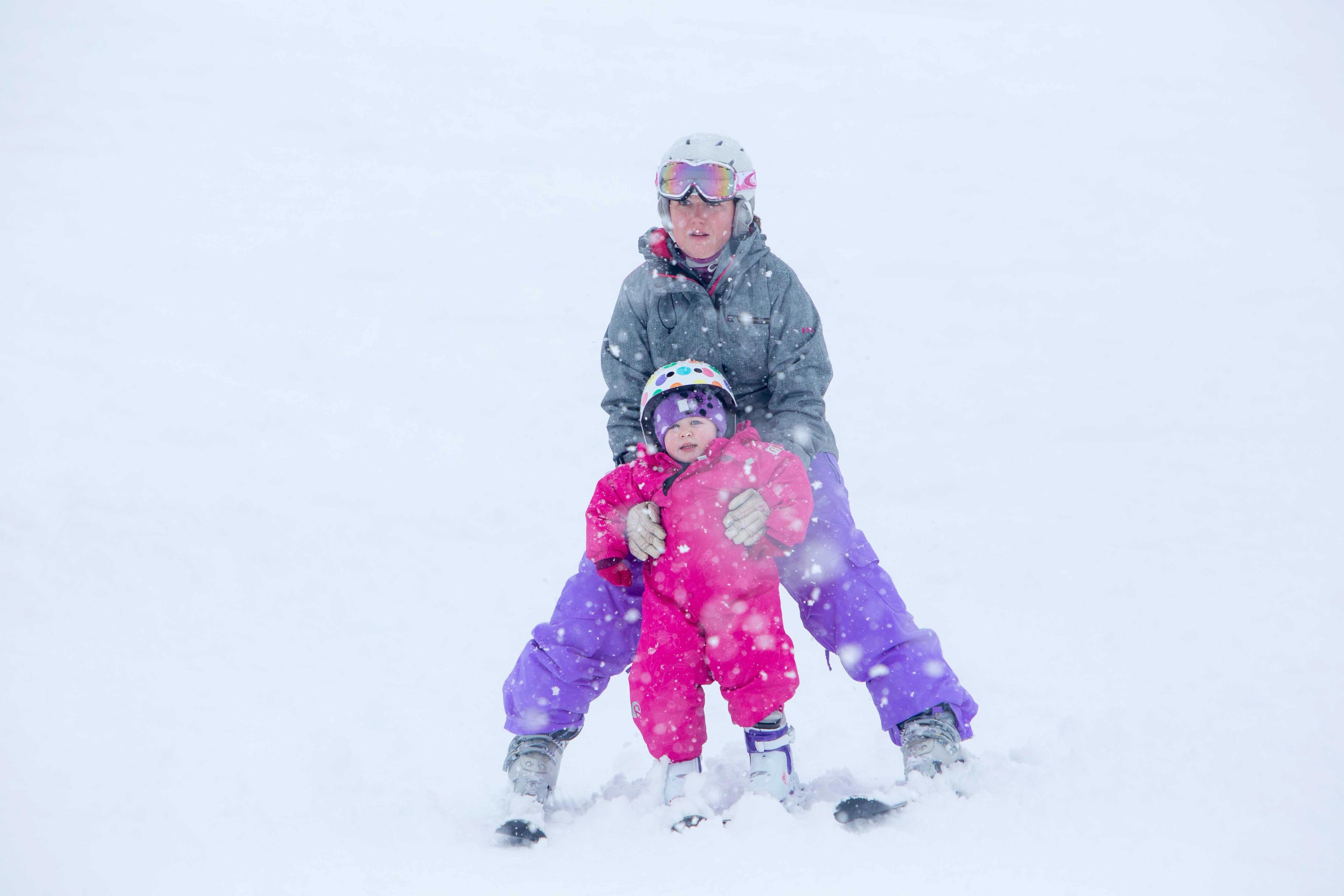 Older child skiing with younger child between legs