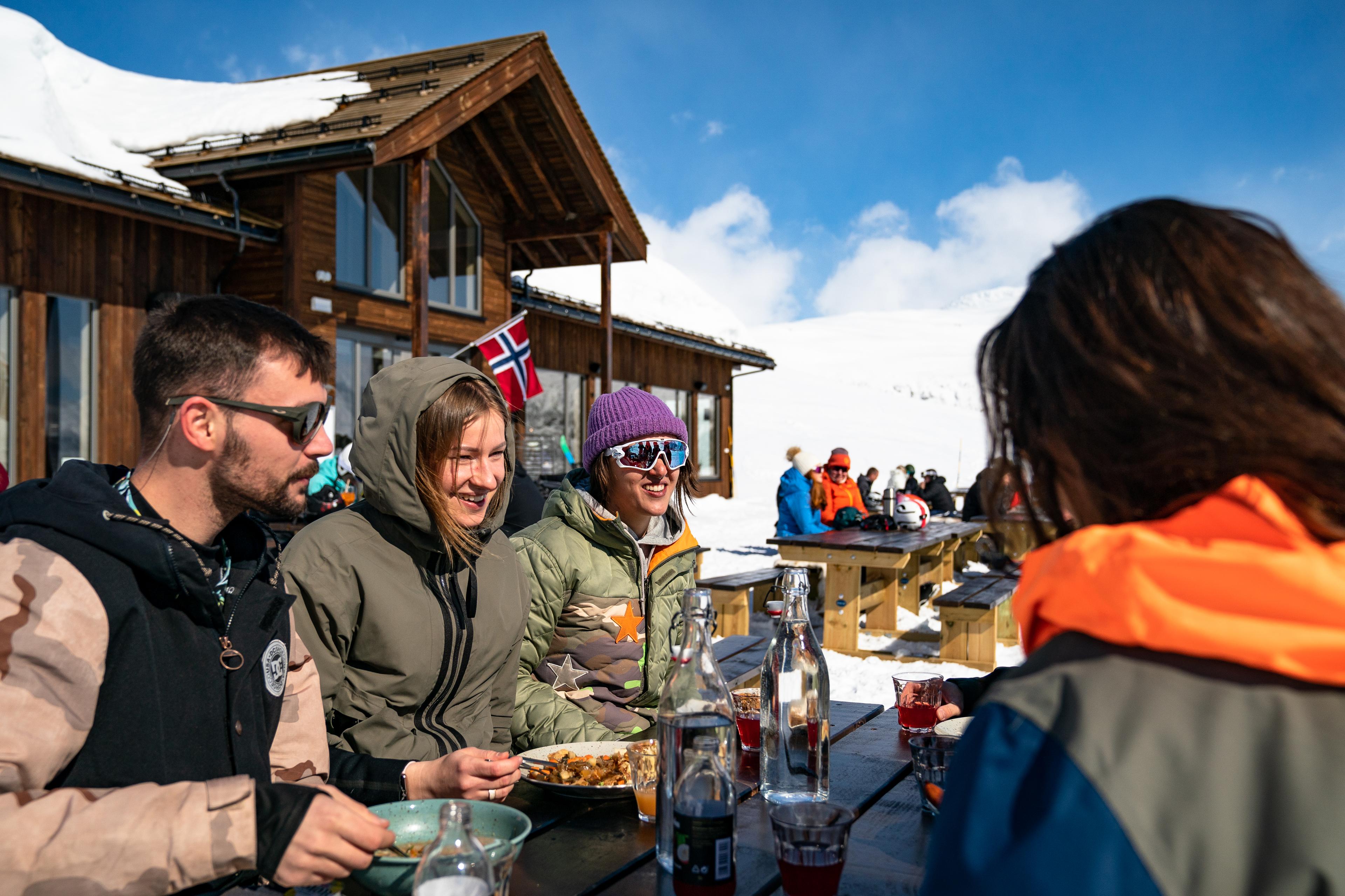 Glade venner sitter på uteservering i bakken og spiser og drikker etter en dag på ski.