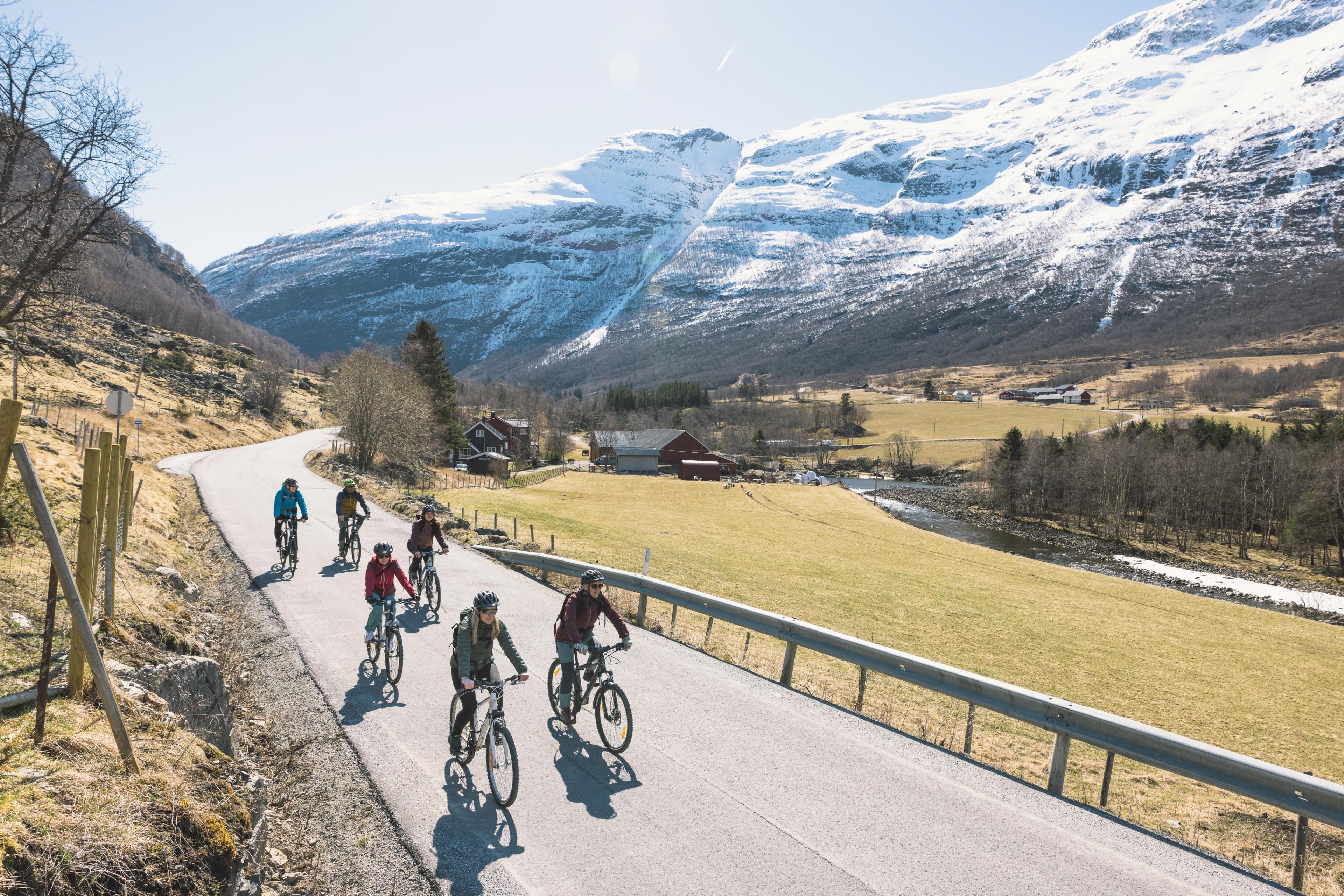 Turister på sykkeltur på Borgund i Lærdal i sol og blant snødekte fjell.
