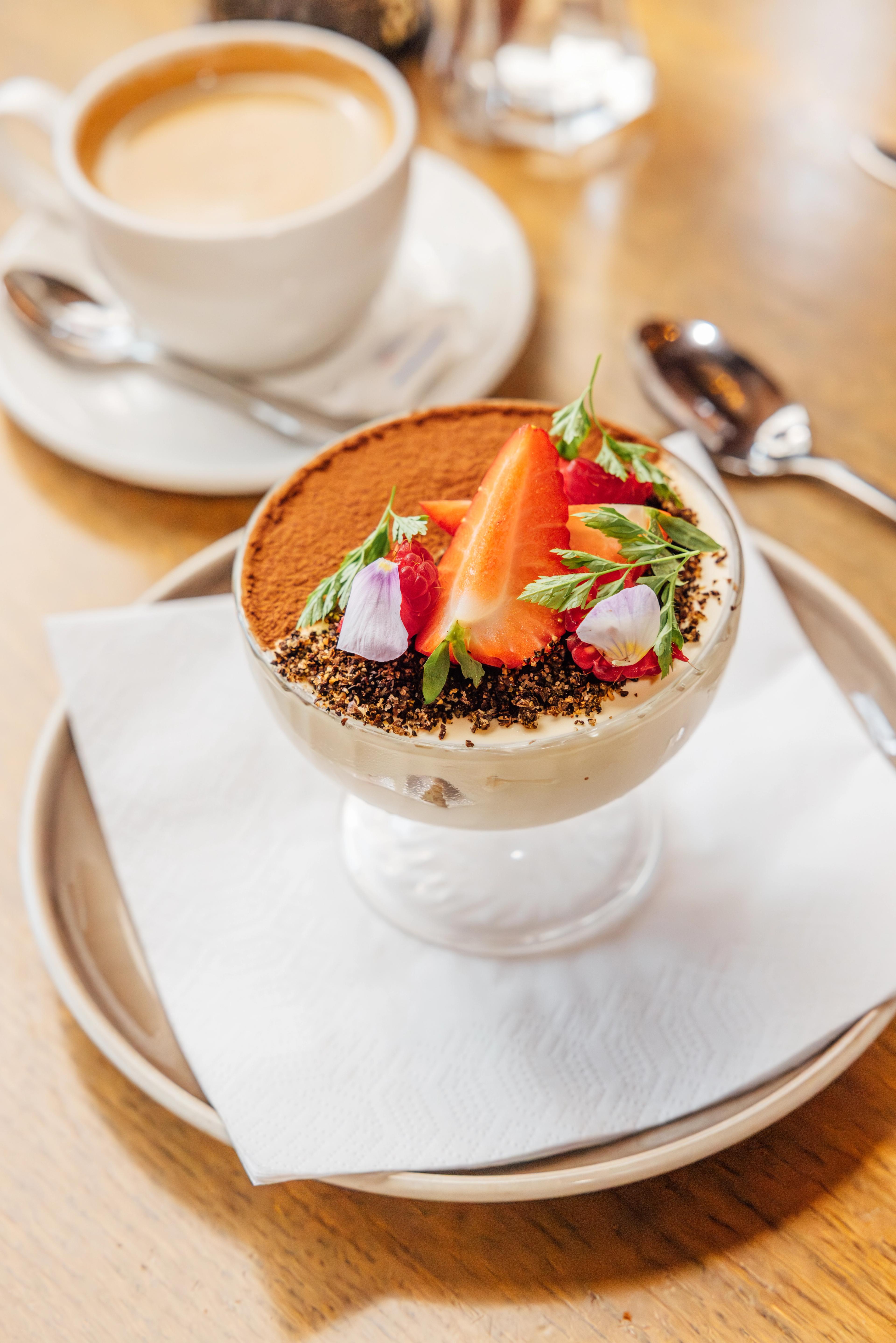 Creamy dessert with strawberry topping and a cup of coffee in the background.