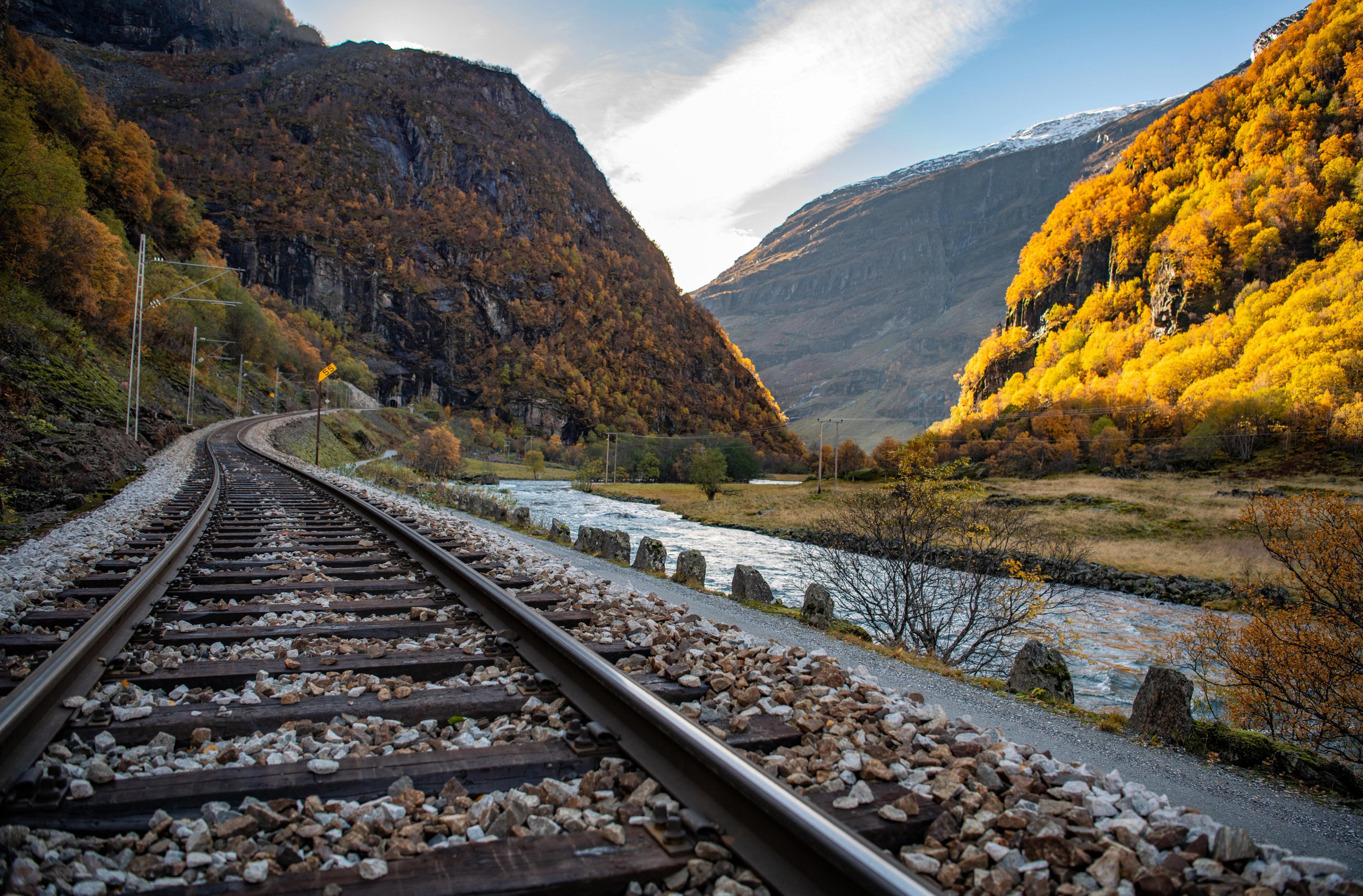 Eisenbahnschienen in einer herbstlich gekleideten Berglandschaft.