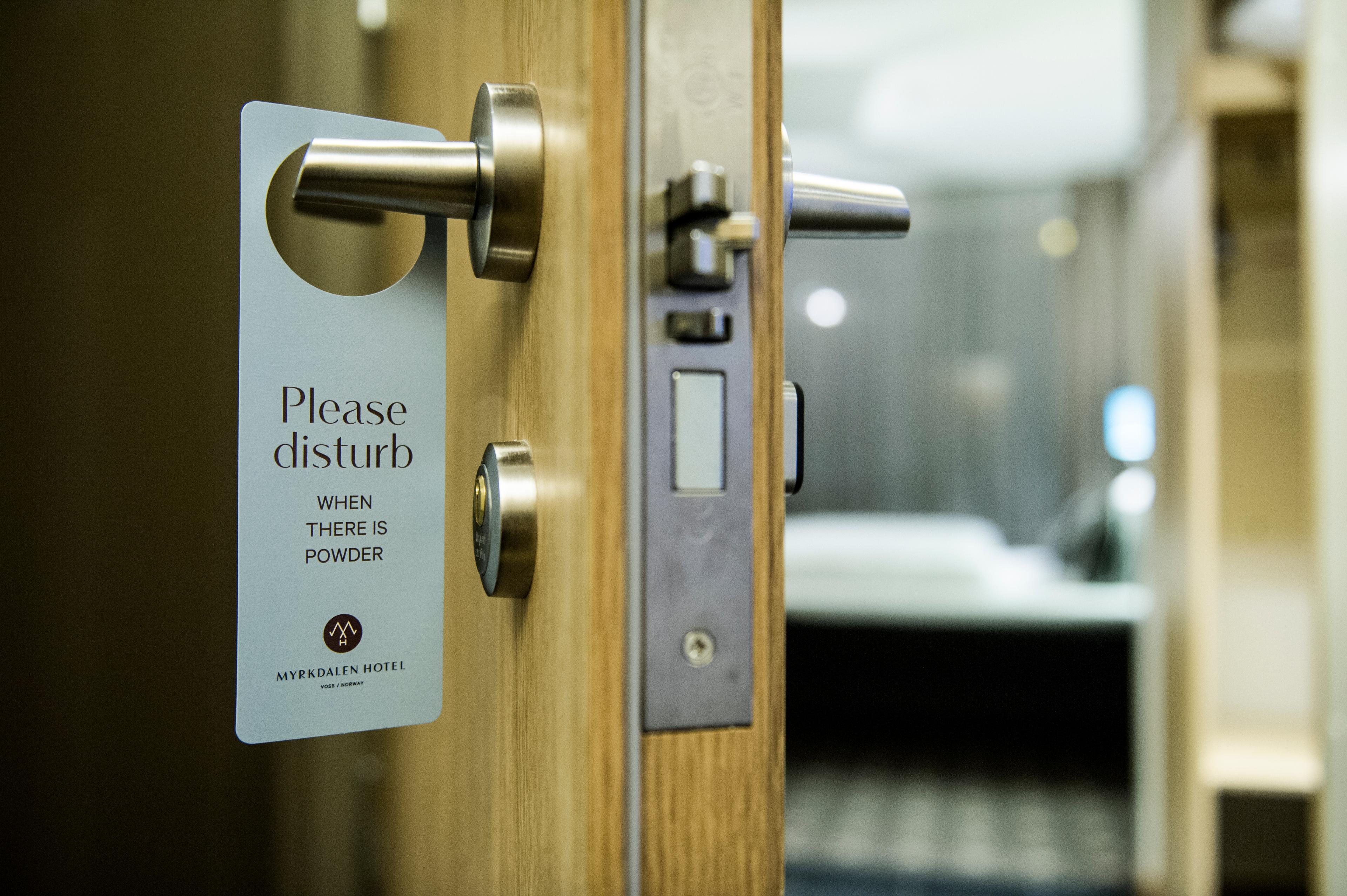 Hotel room door ajar with a sign on the door handle that reads "Please disturb when there is powder".