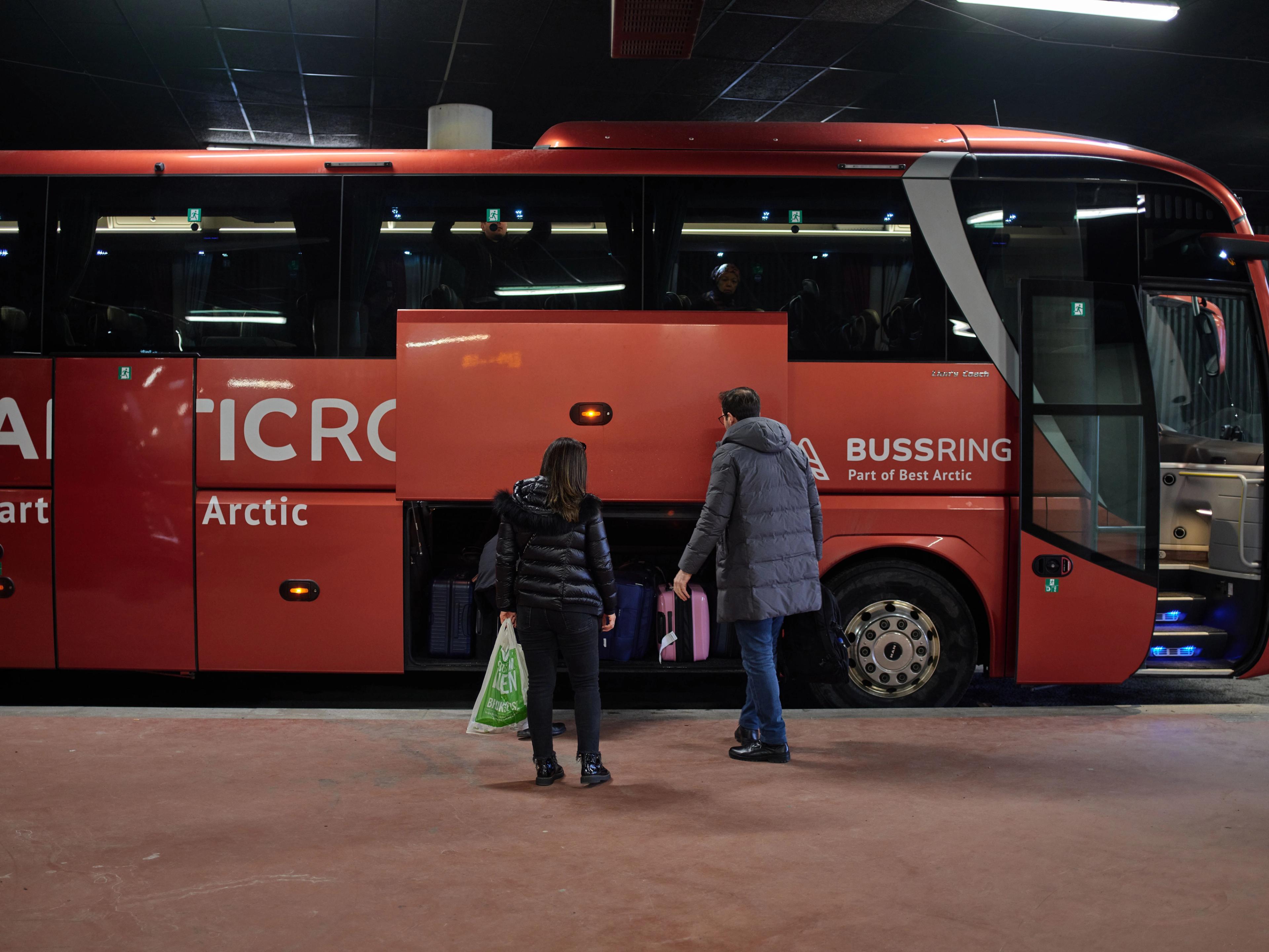 Deux personnes avec des bagages se dirigent vers un bus rouge Arctic Route.