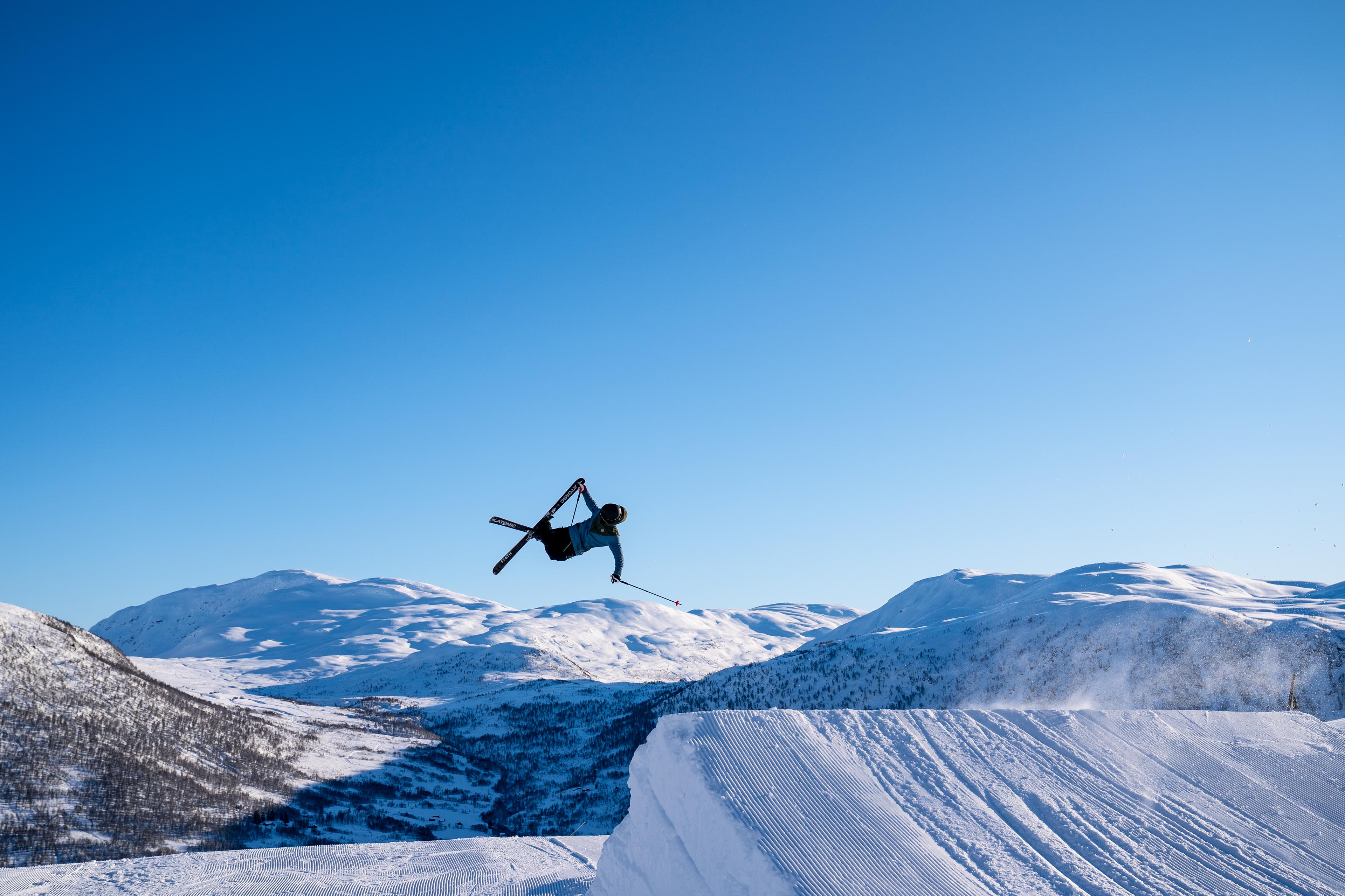 Person hopper på ski med fjellene i bakgrunnen