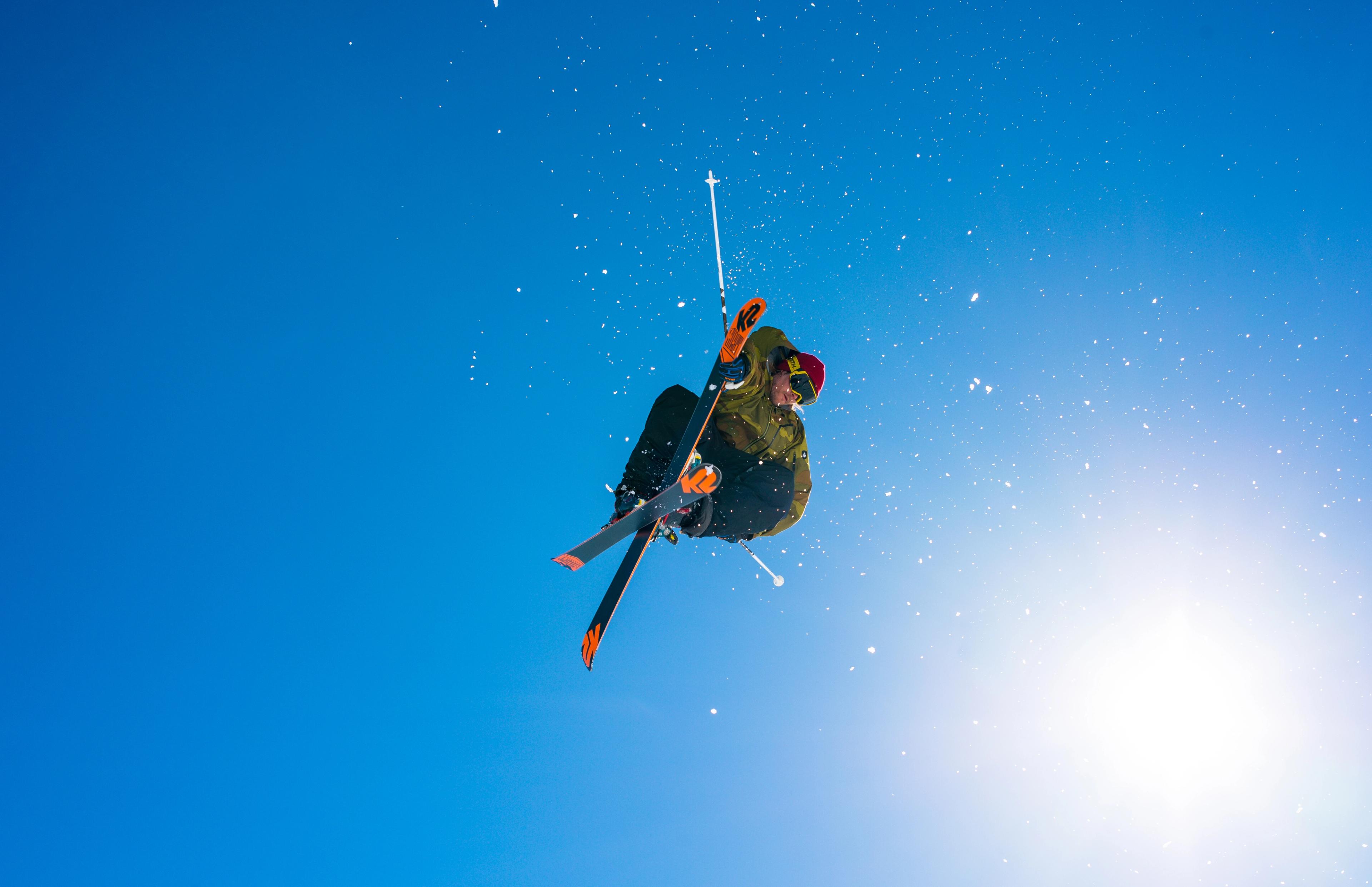 A skier in the air with the sun and a blue sky in the background