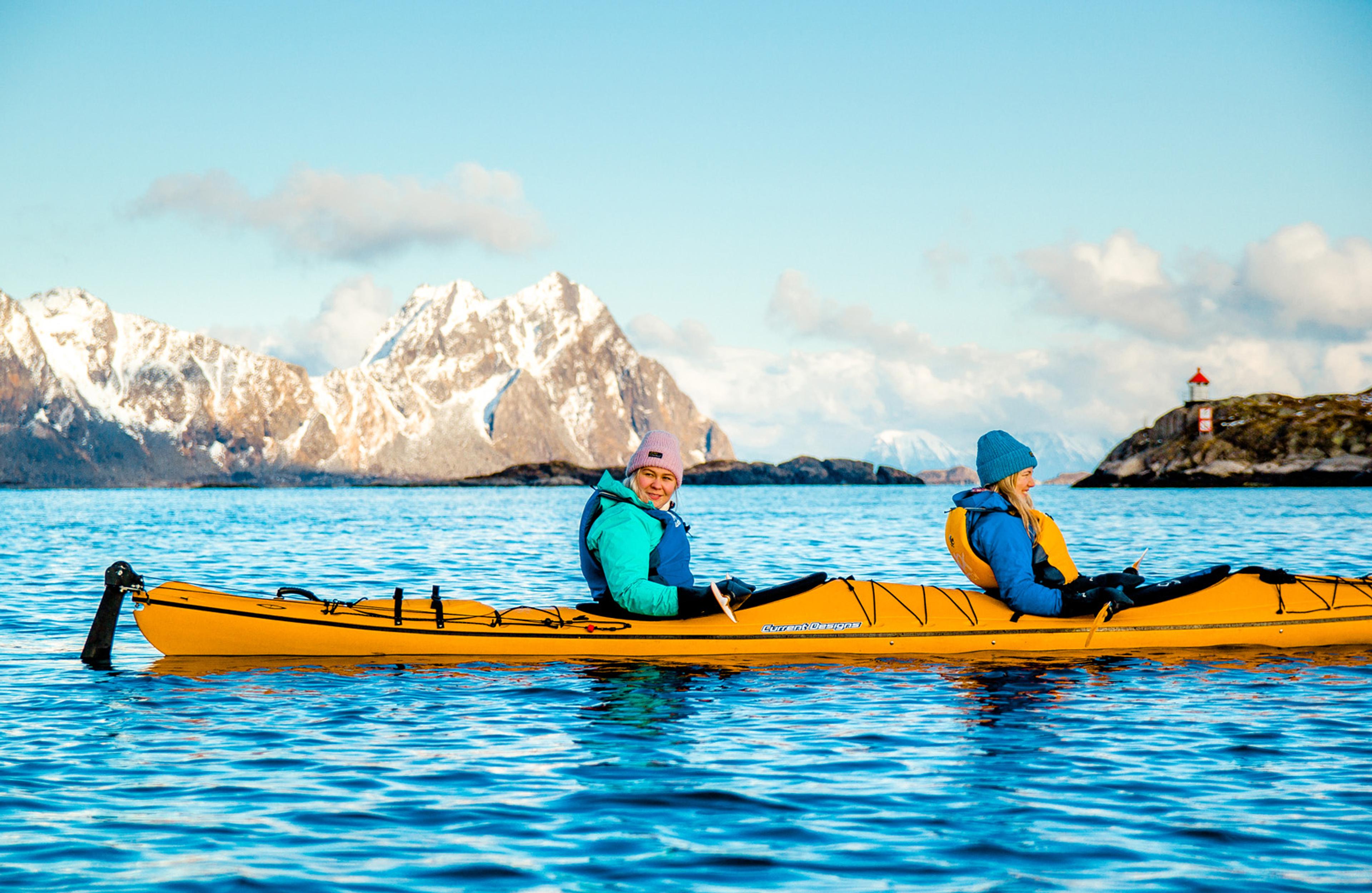 Two ladies paddling on the sea with snow-capped mountain peaks on the horizon