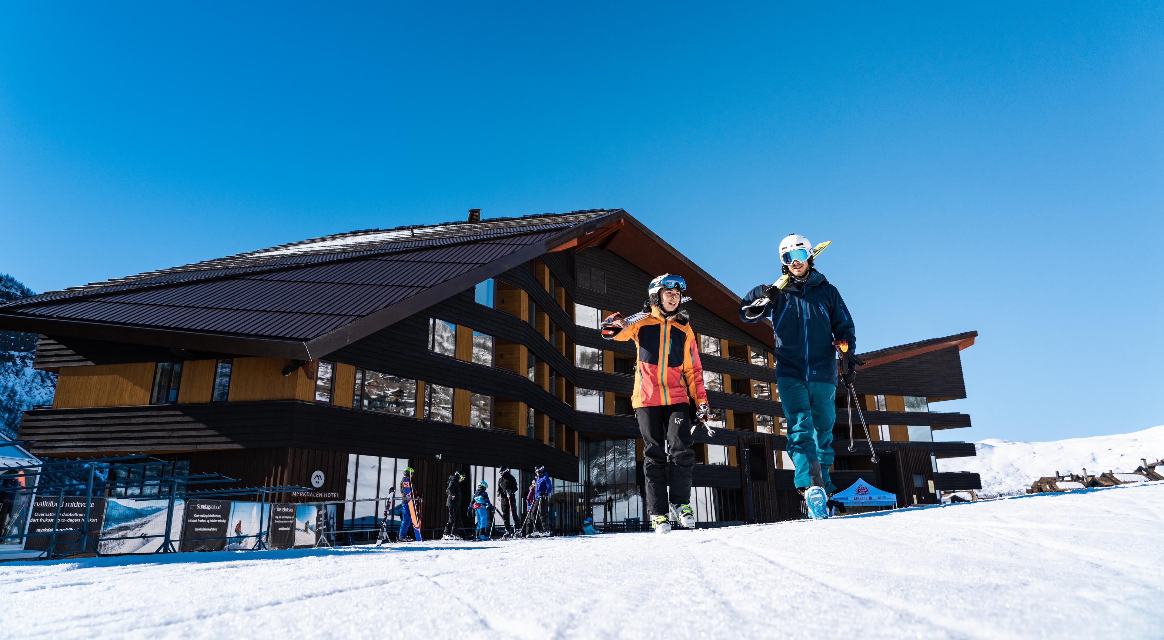 Et par skal ut og stå på ski og bærer slalåmskiene på vei ut fra Myrkdalen hotel.
