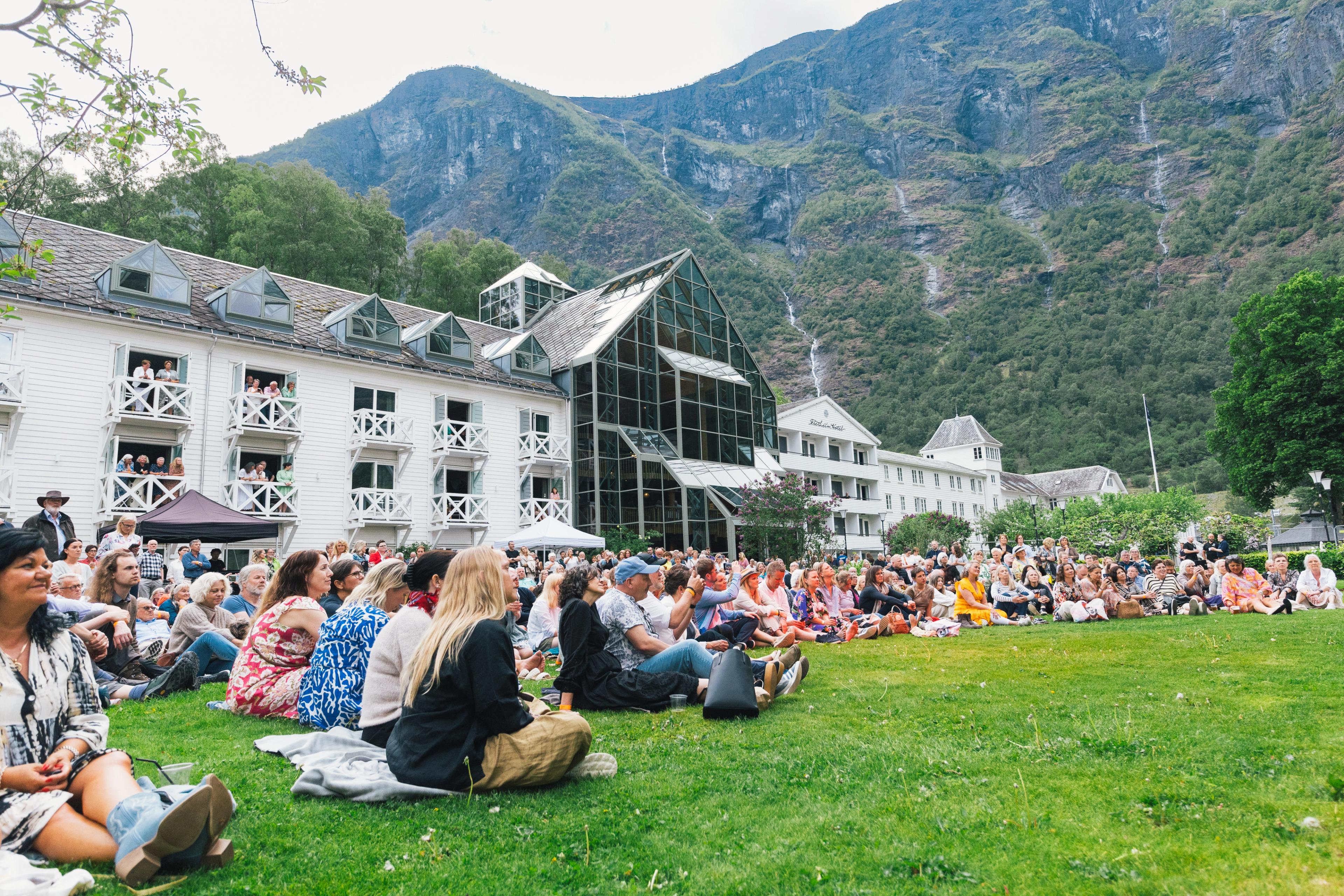Publikum sitter på plenen foran Fretheim Hotel og lytter til musikk på hagekonserten.