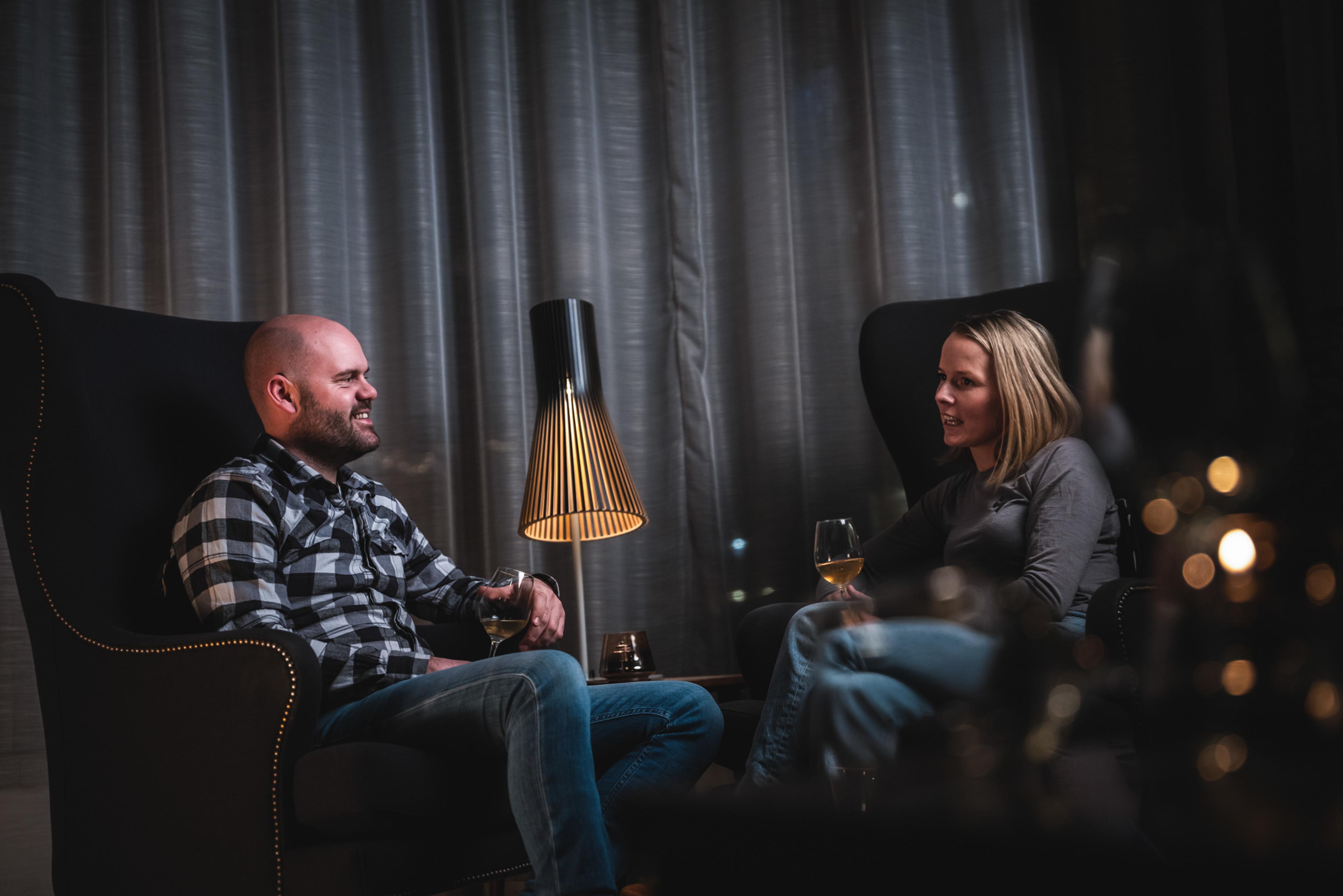 Two people enjoy themselves in armchairs with a glass of wine