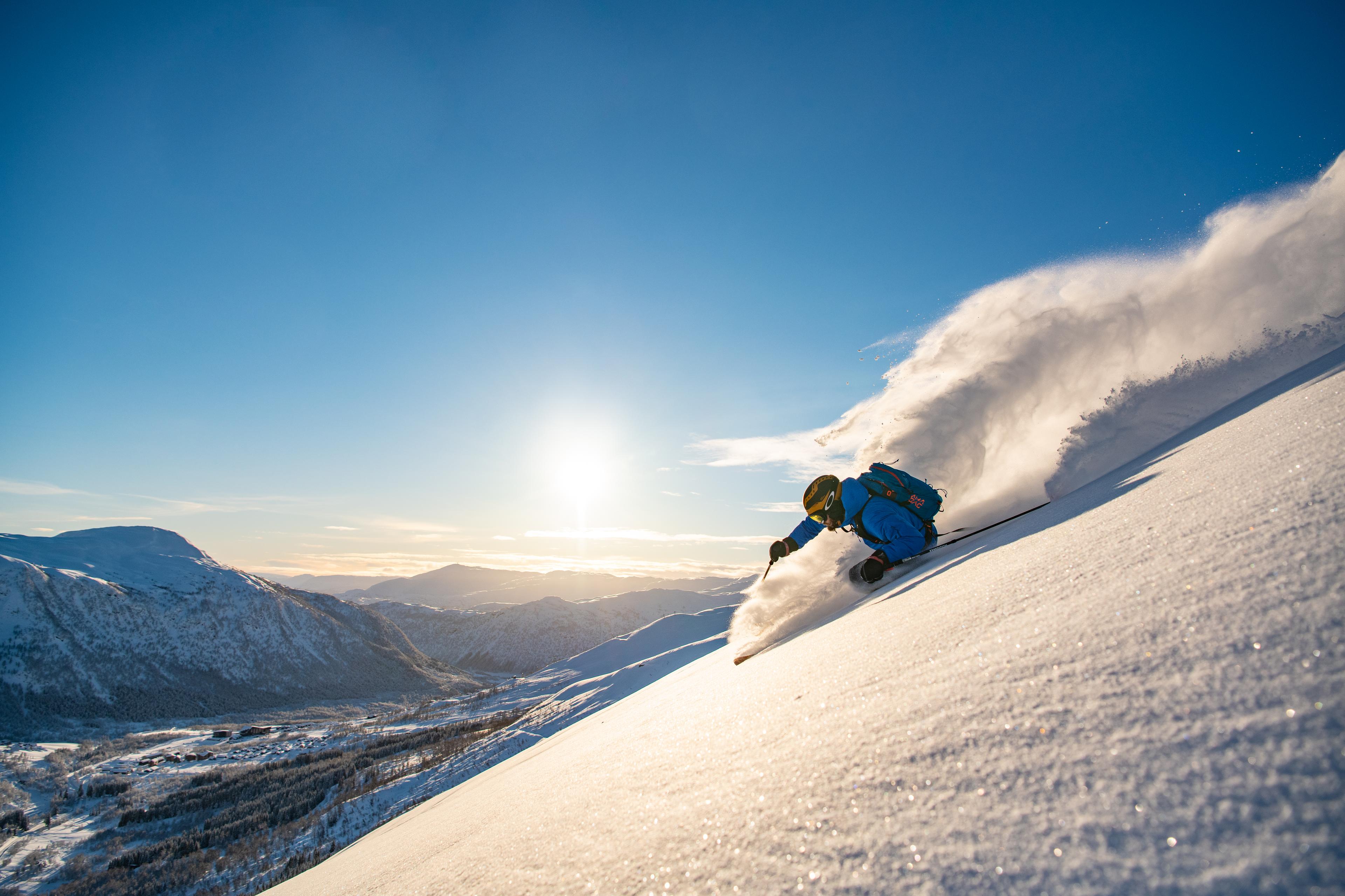 Skiløpar frikøyrer ned den bratte fjellsida så snøføyka står.