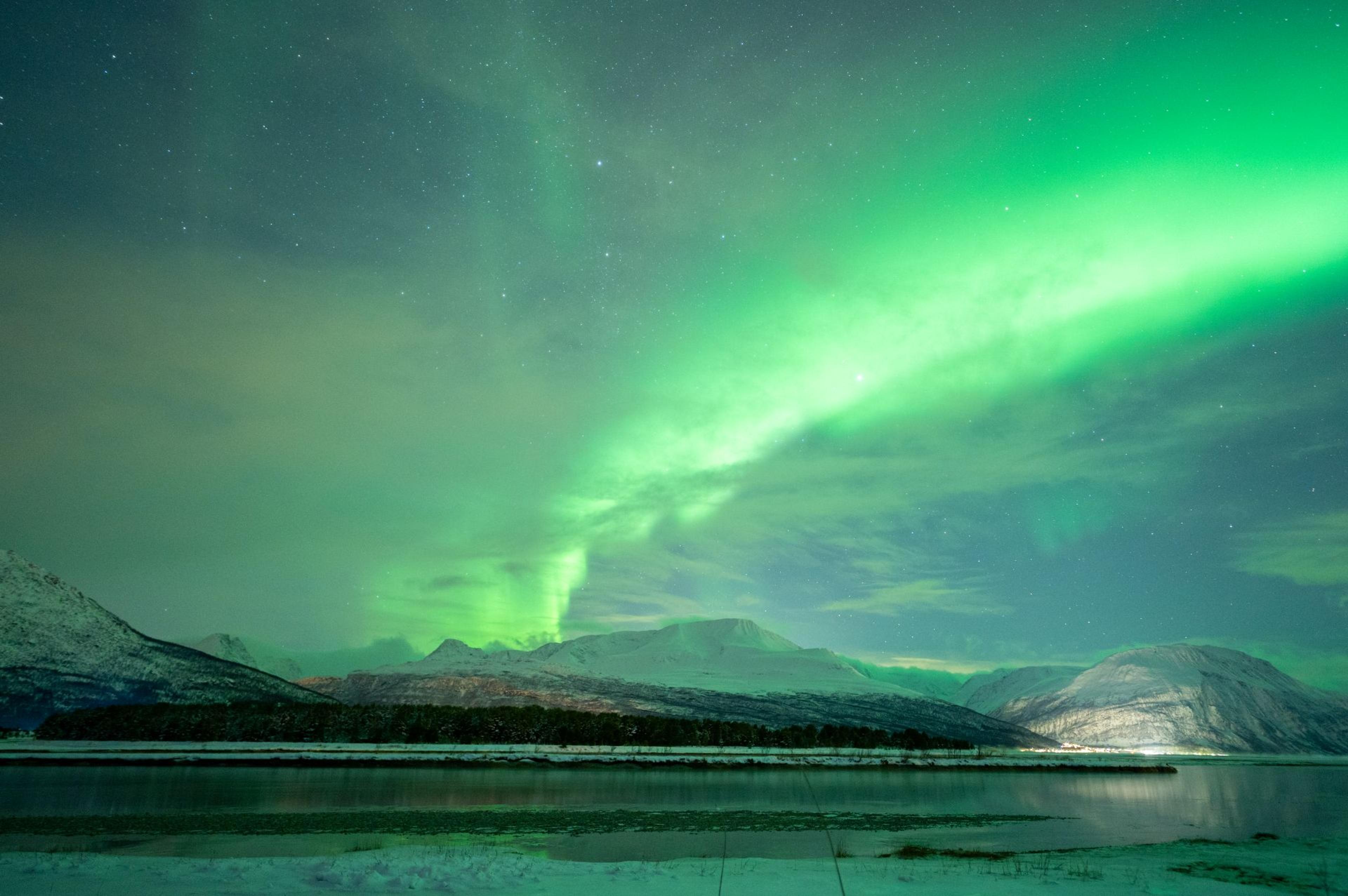 Green Northern Lights over a snow-covered fjord and mountain landscape near Narvik.