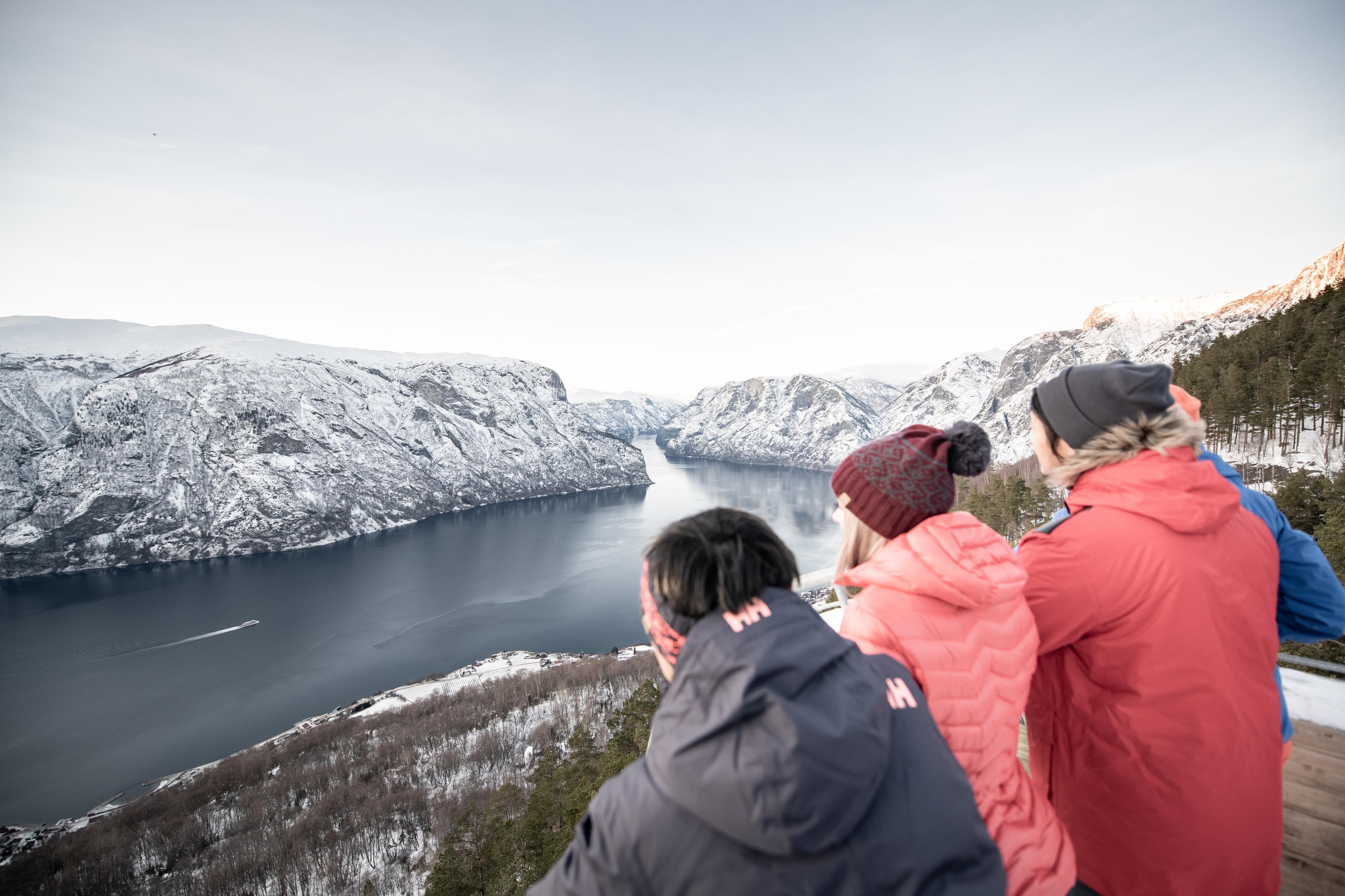 Venner på tur står ytterst på plattformen og ser ned over fjorden fra Stegastein.