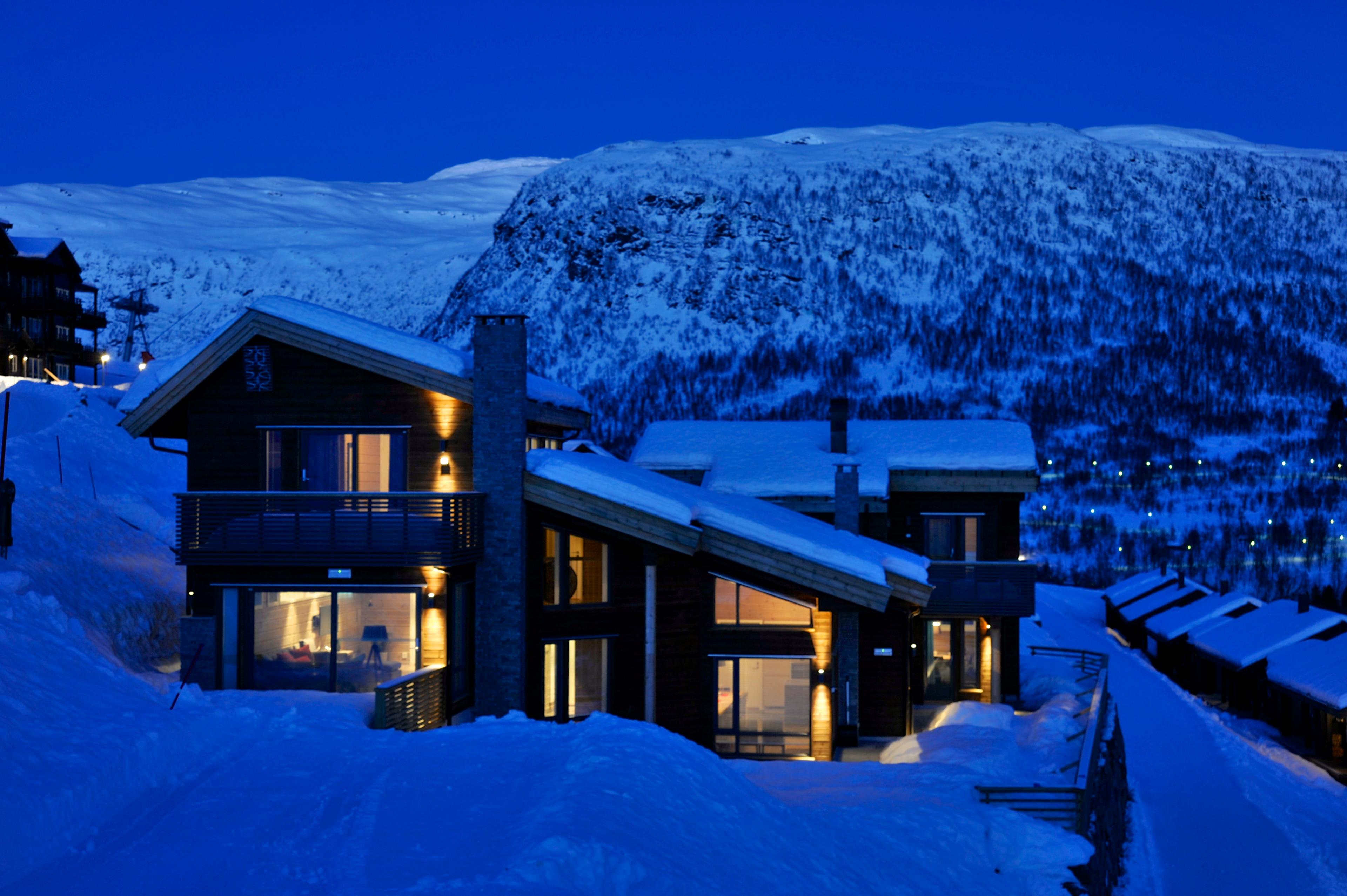 Koselig stemning om kvelden med lys fra hyttene og snø.