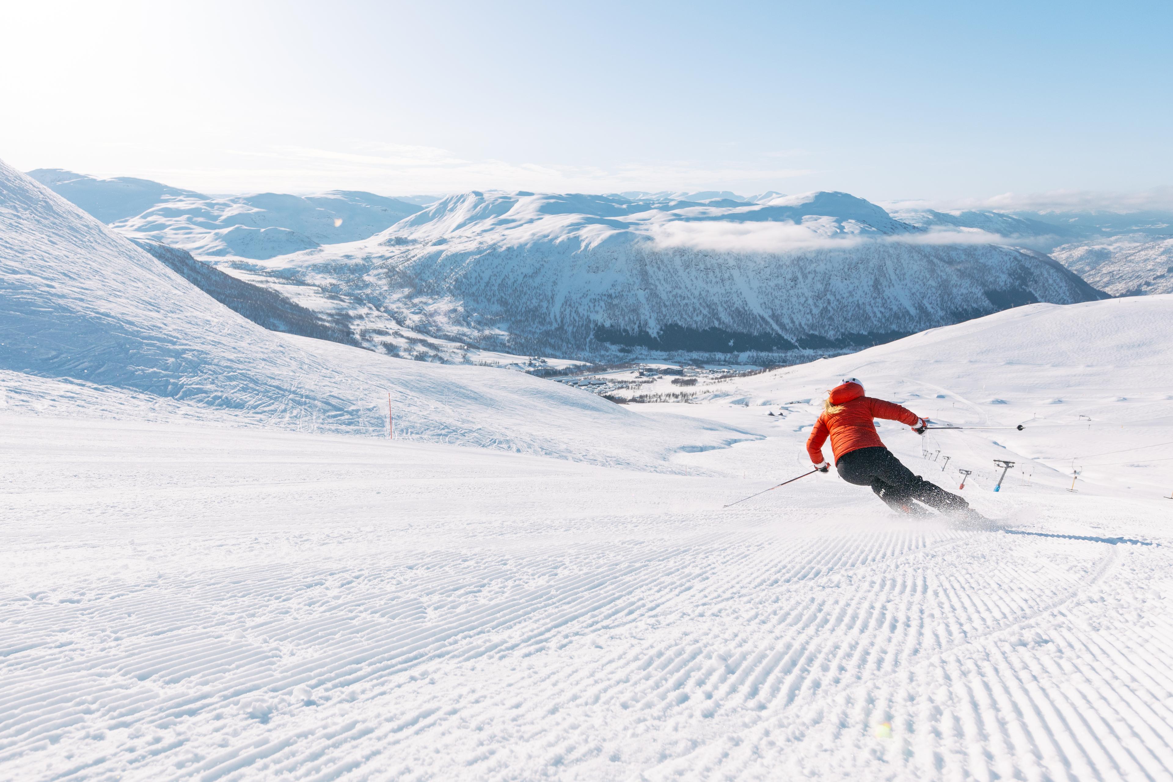 Person står på slalåm nedover en bakke med fjell i bakgrunnen