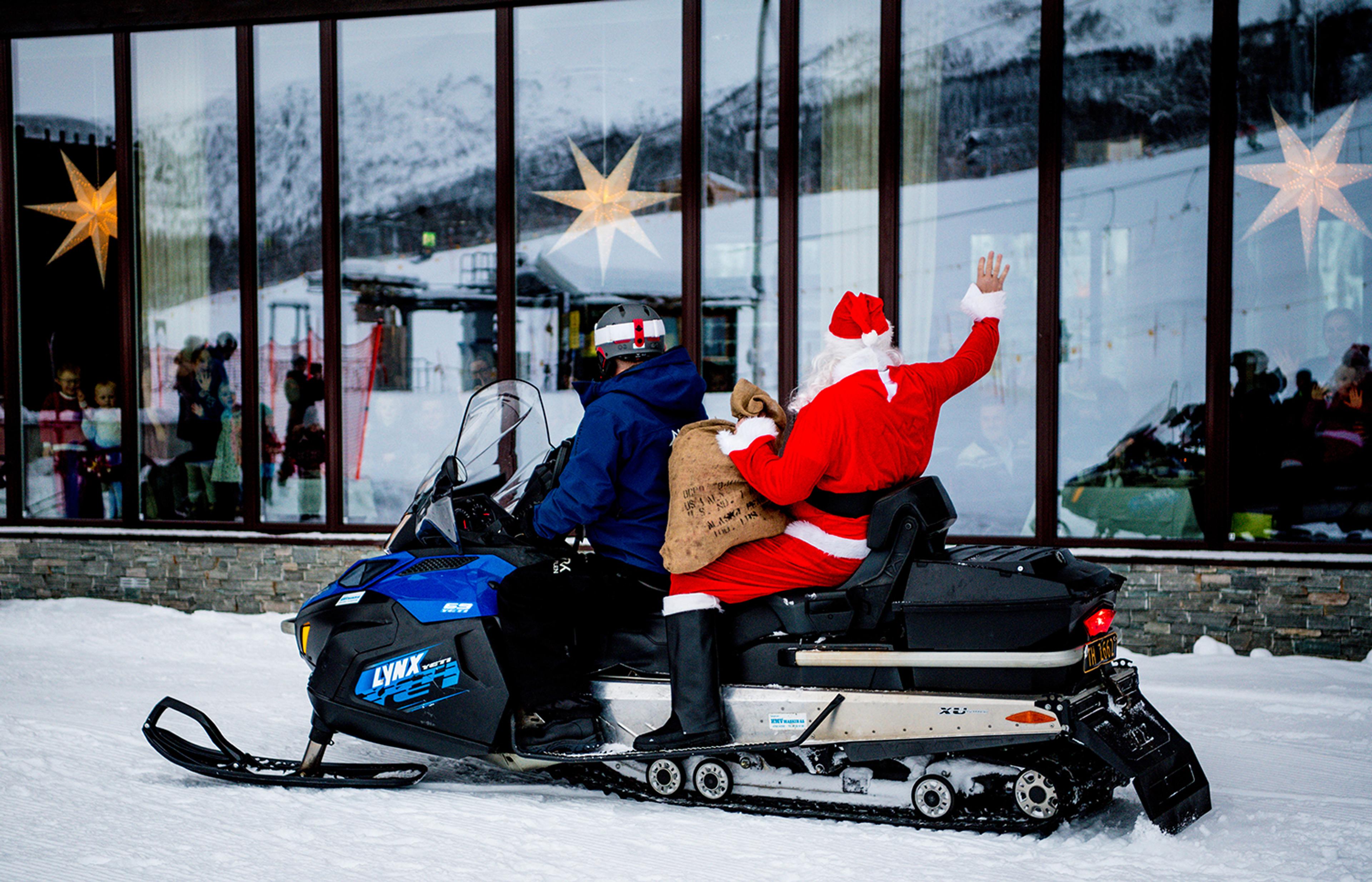 A Santa Claus on a snowmobile waves to the guests sitting inside the restaurant