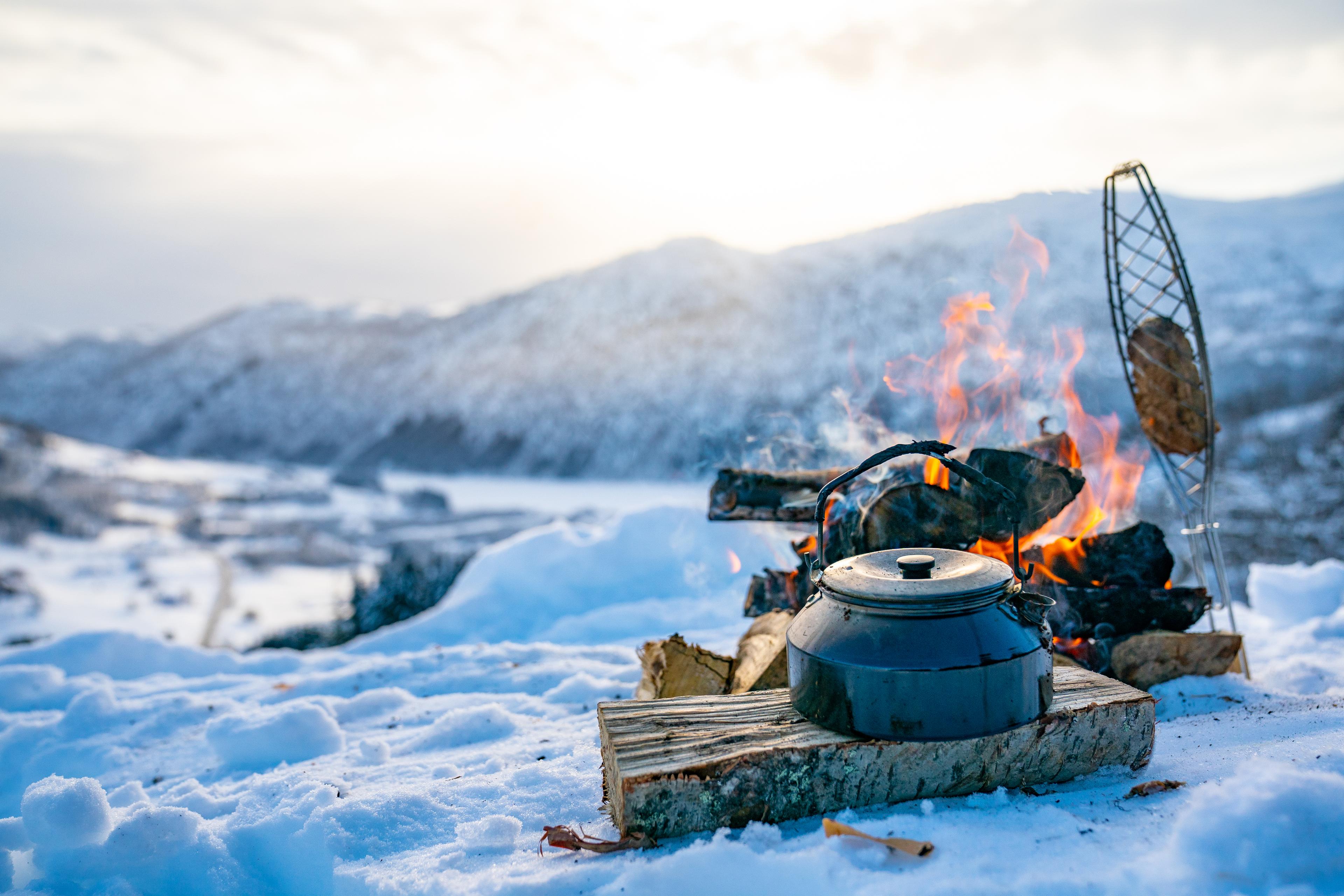 Mat og drikke tilberedes på bål i snøen.