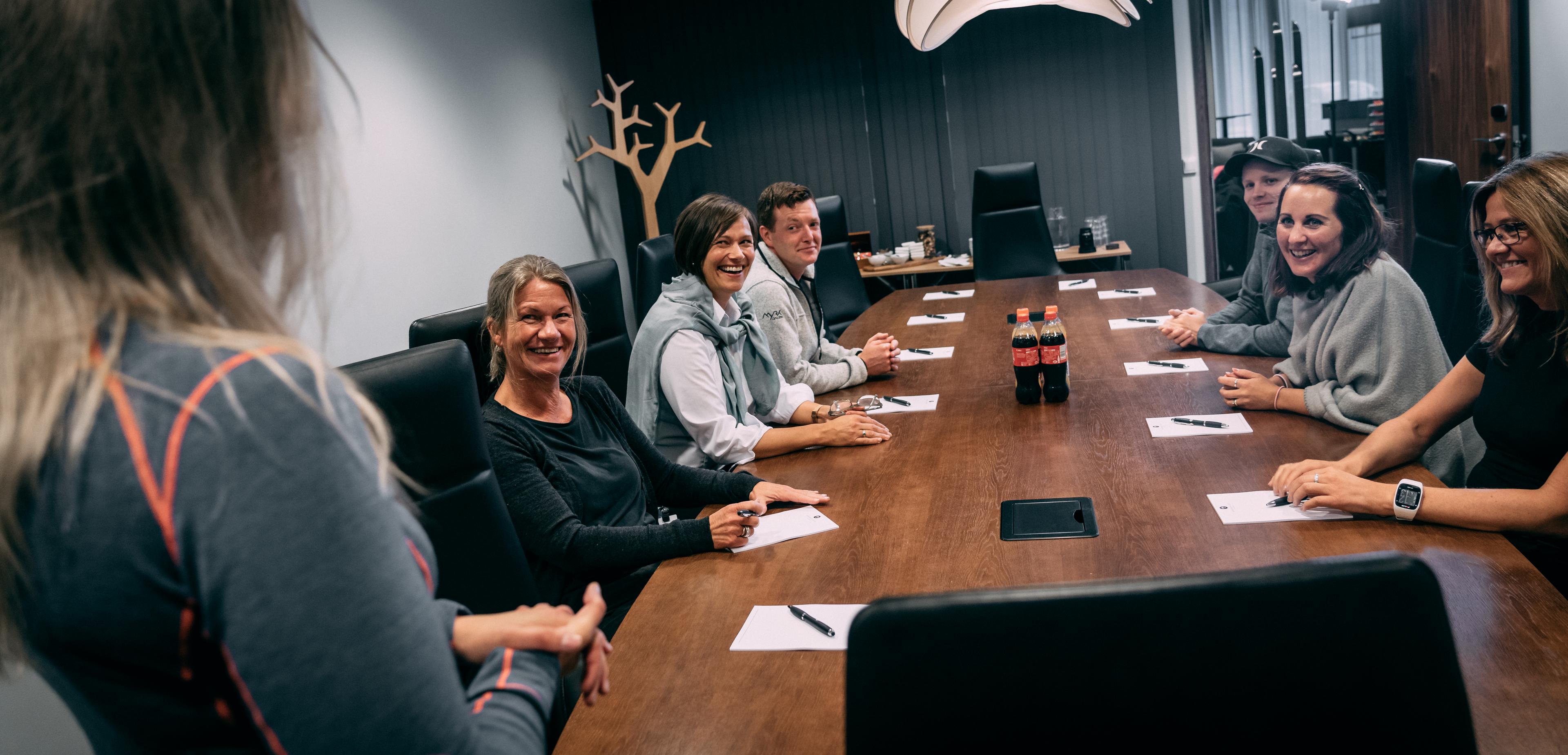 A group of people are sitting around a large table inside a meeting room