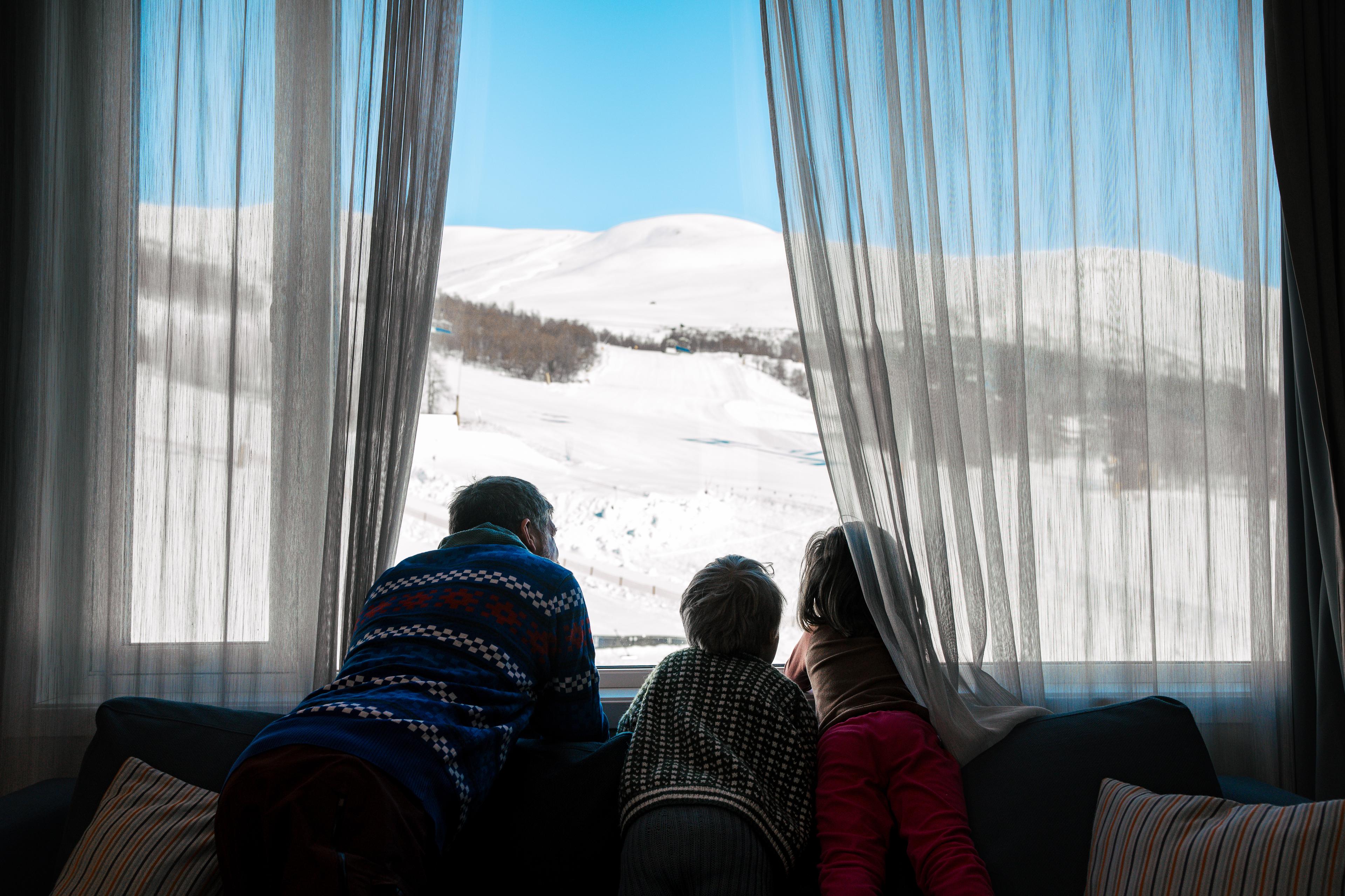 Father and two children look out over the ski slope from their hotel room window.