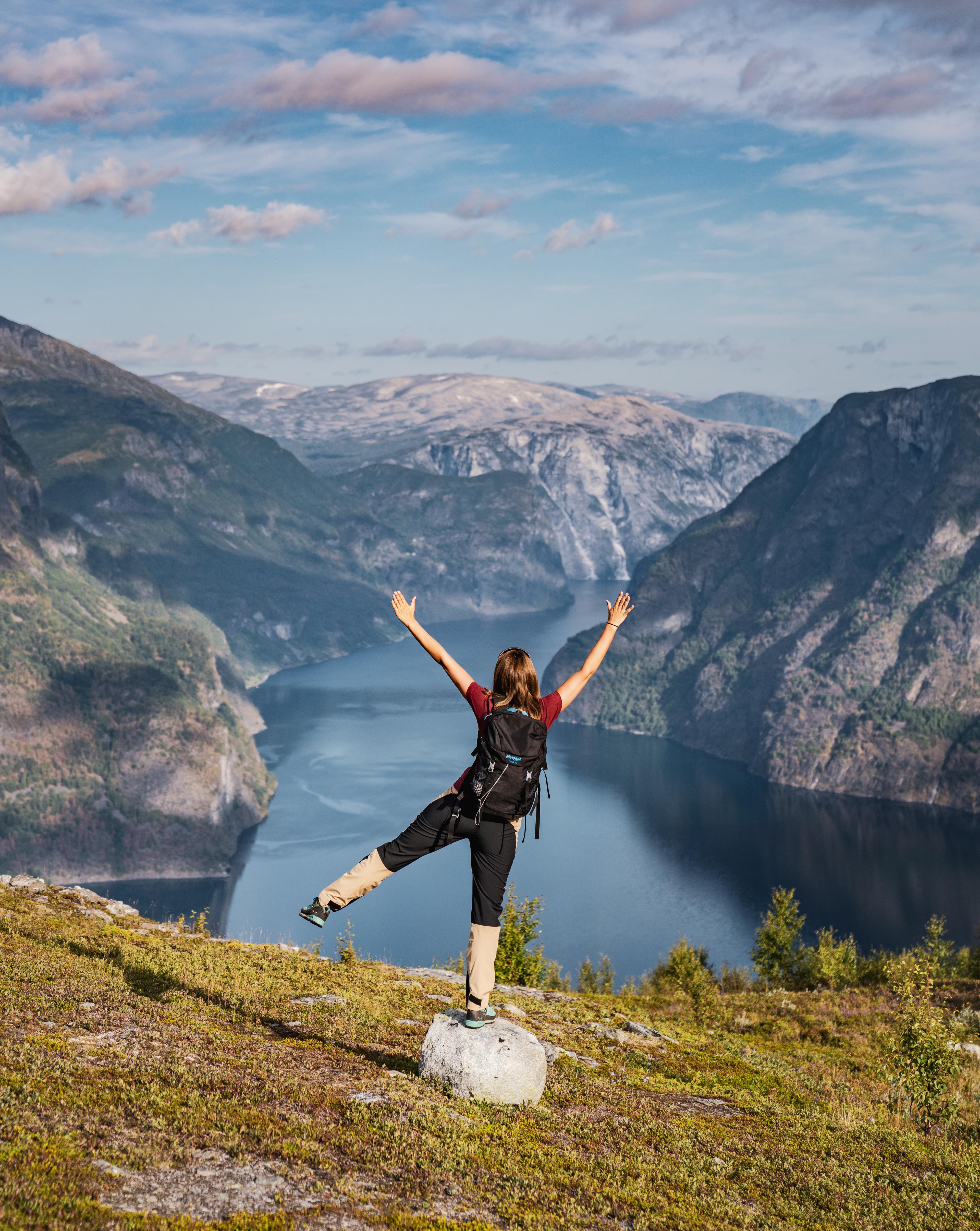 Ei jente balanserer på en stein med panorama over Aurlandsdalen på vei opp til Prest.