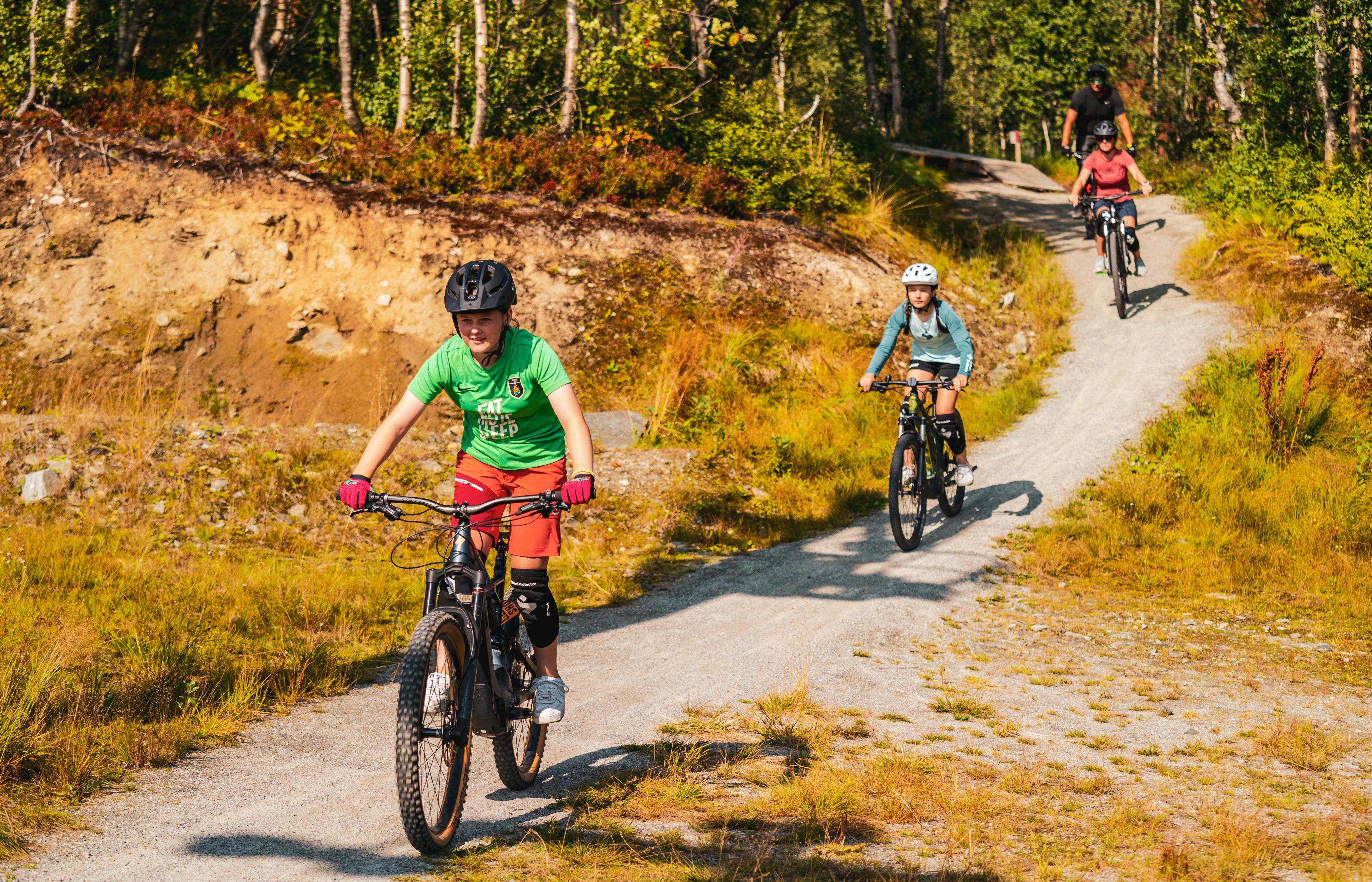 En familie kommer syklende nedover en grussti i skogen.