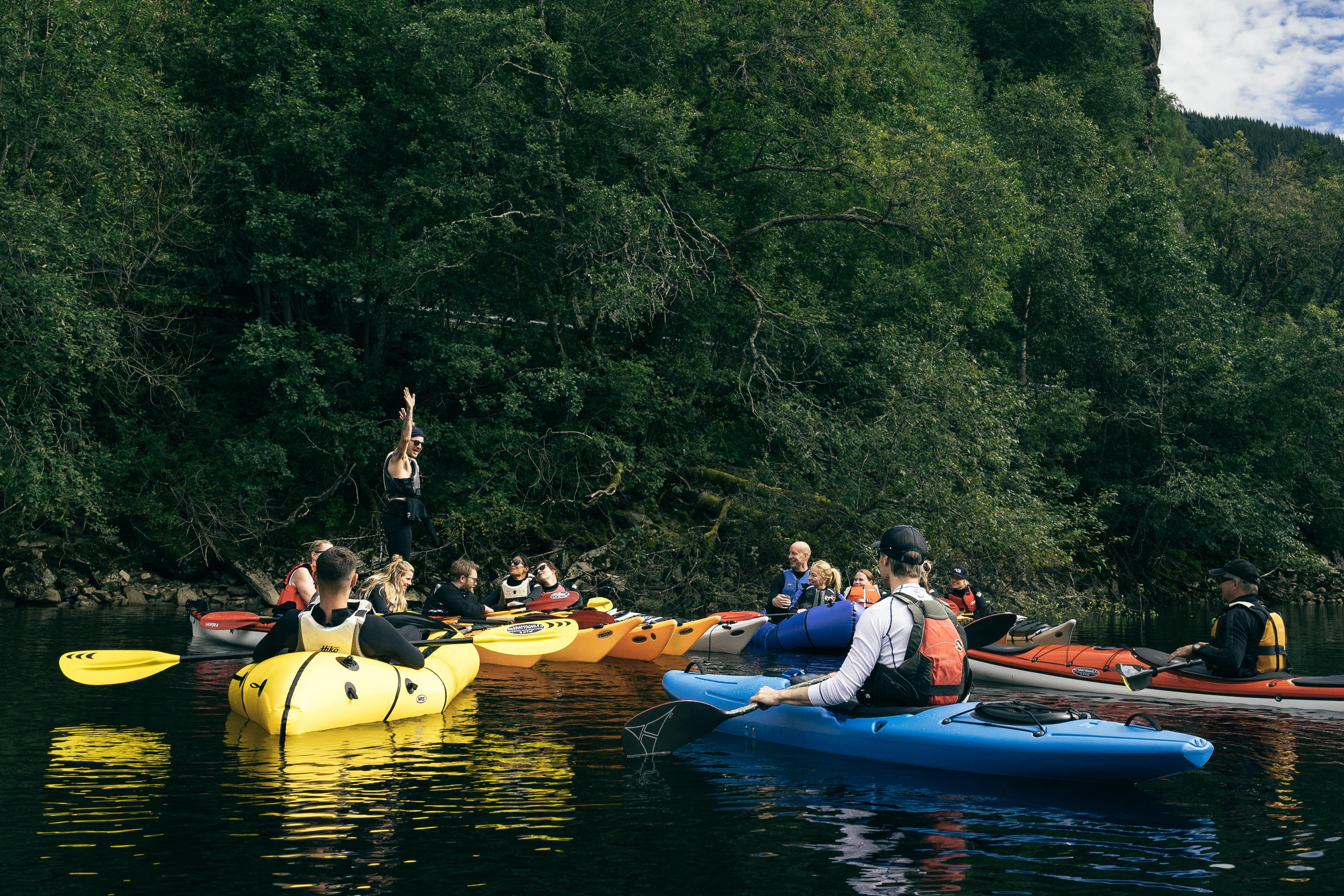En gruppe mennesker i kajakker samles på elva og får informasjon av guiden.