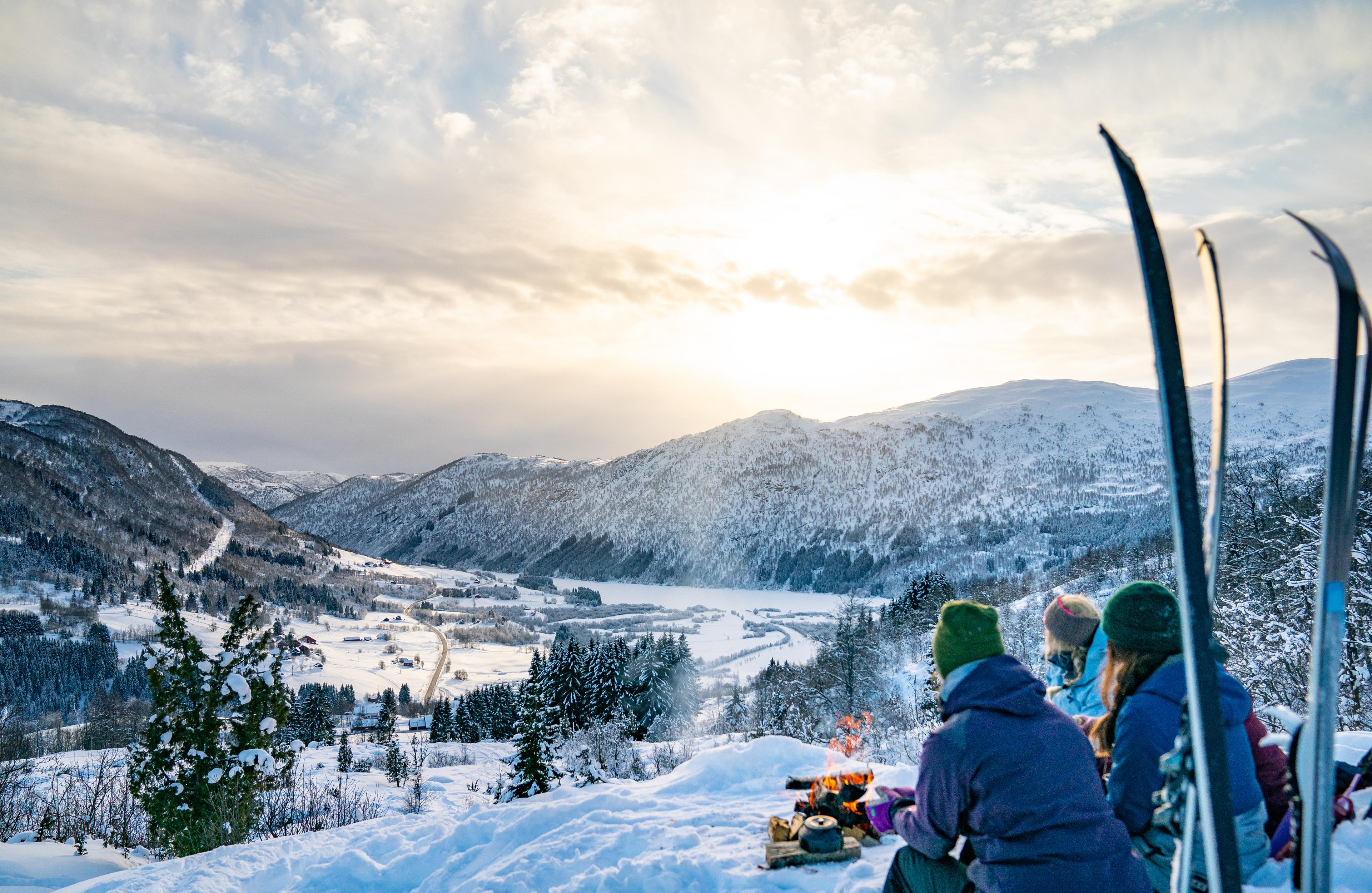 A group on a ski trip sits in front of the fire and looks out over the valley.