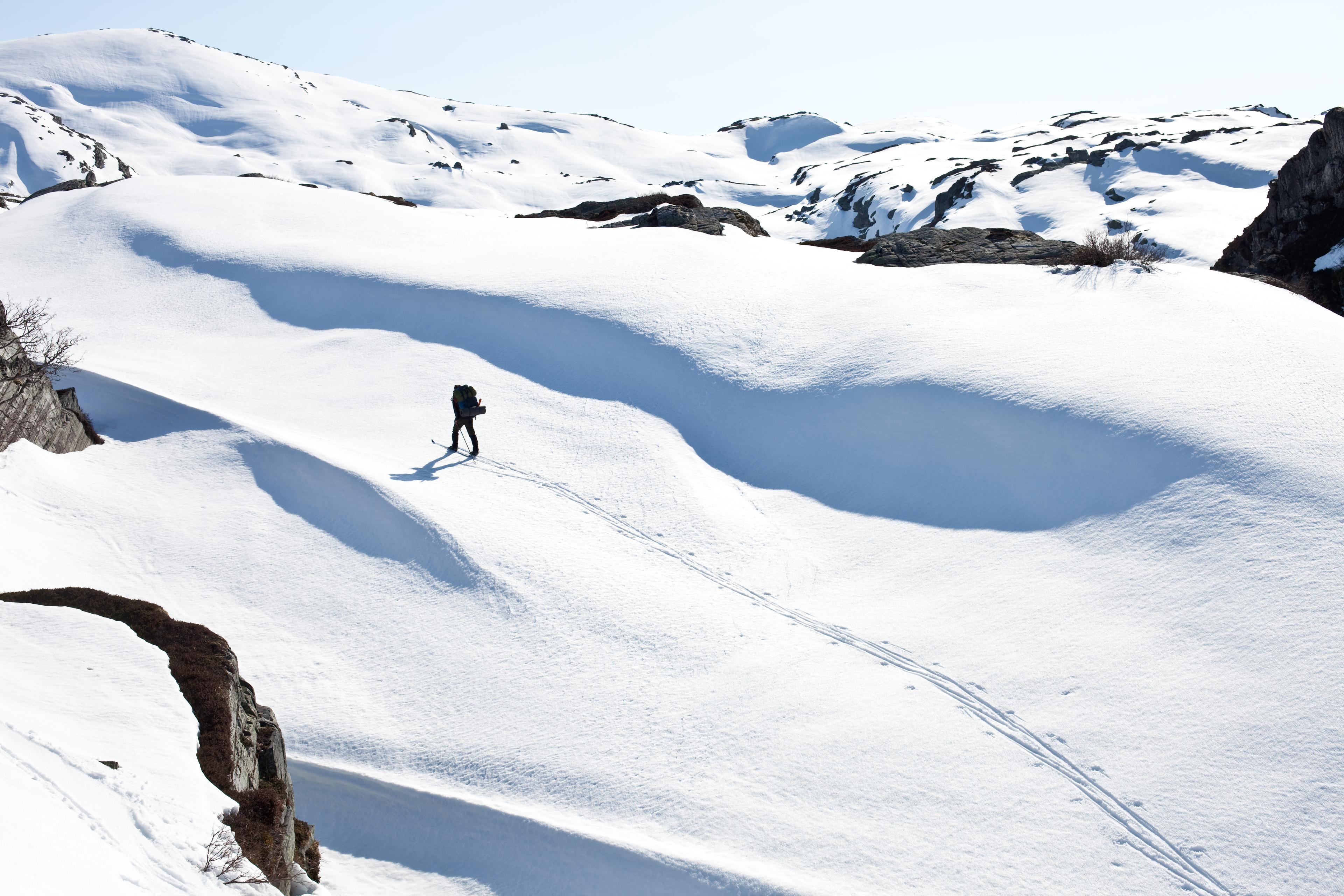 En skiløper går alene på fjellski oppover fjellet i nysnø og solskinn.