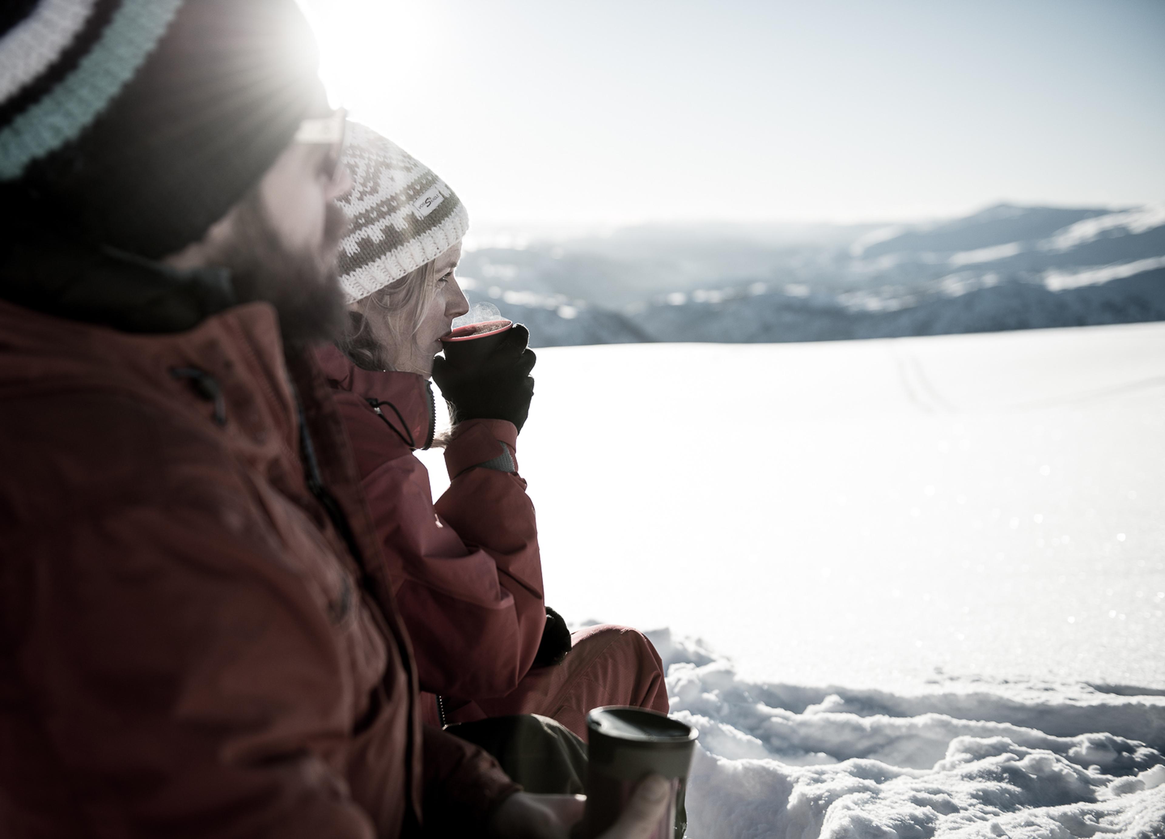  A couple out on a winter walk are sitting and enjoying the sun and something hot in their cup.