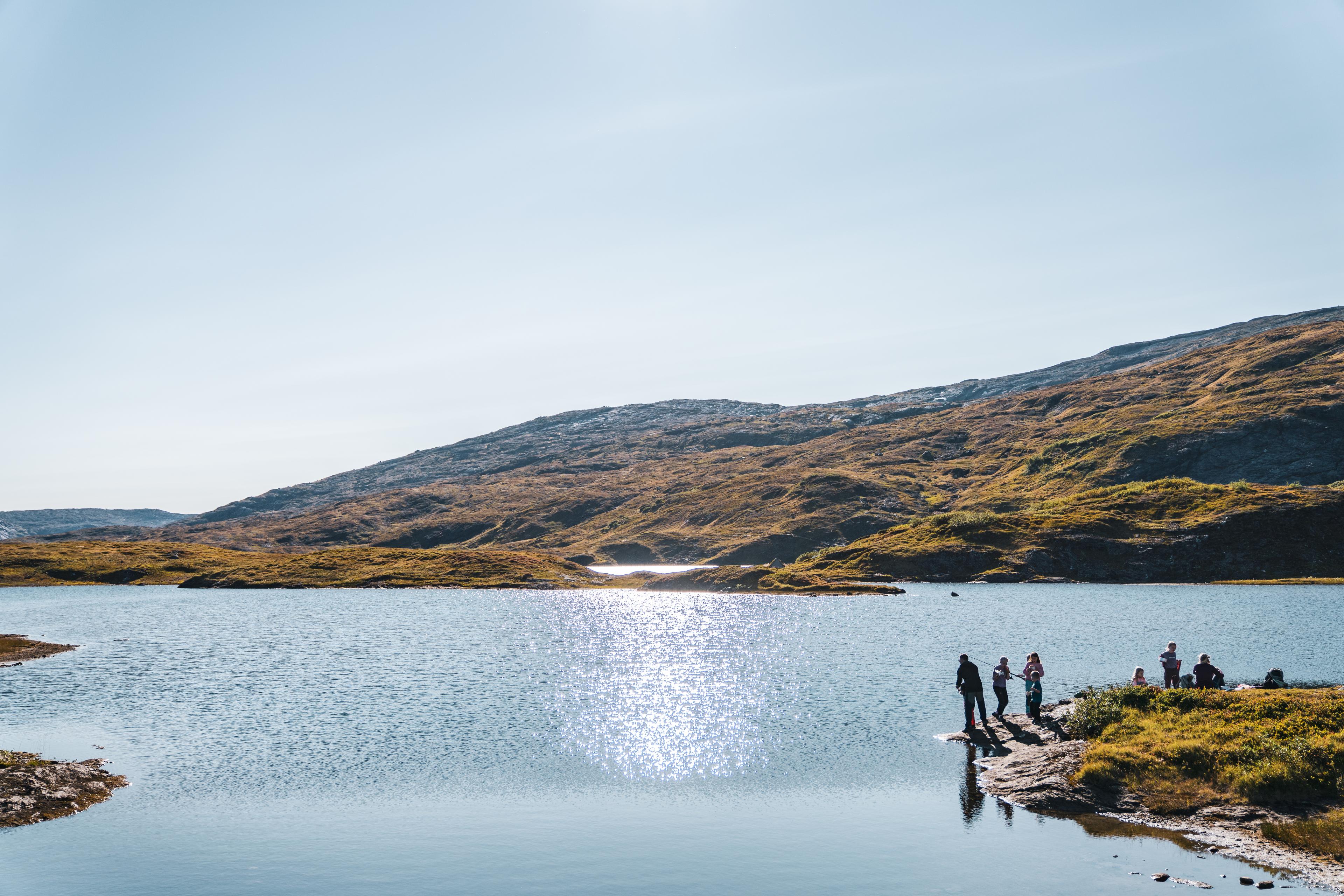 En gruppe fisker i et fiskevann på fjellet i solskinn.