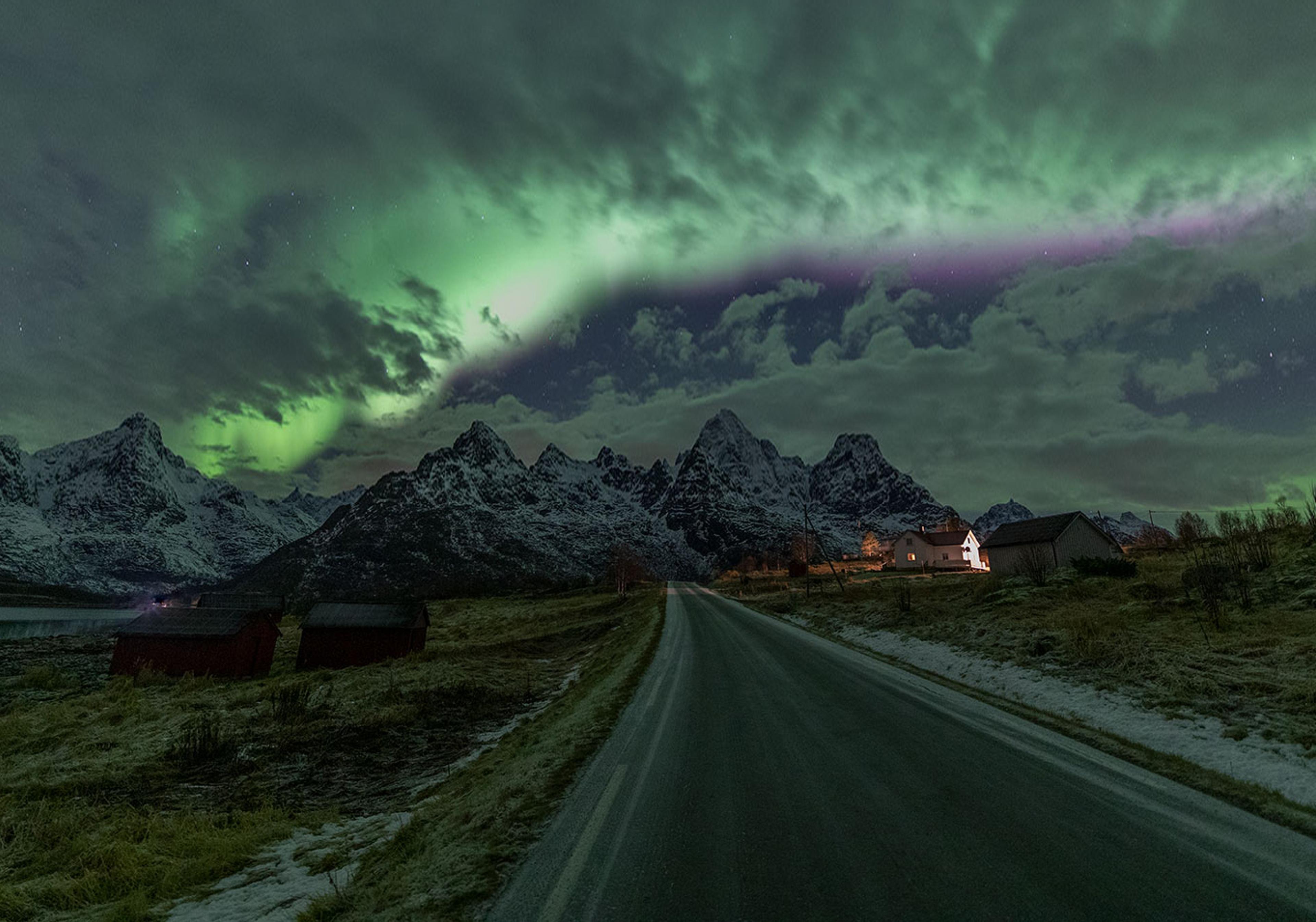 Nordlichter am bewölkten Himmel über einer schneebedeckten Bergkette