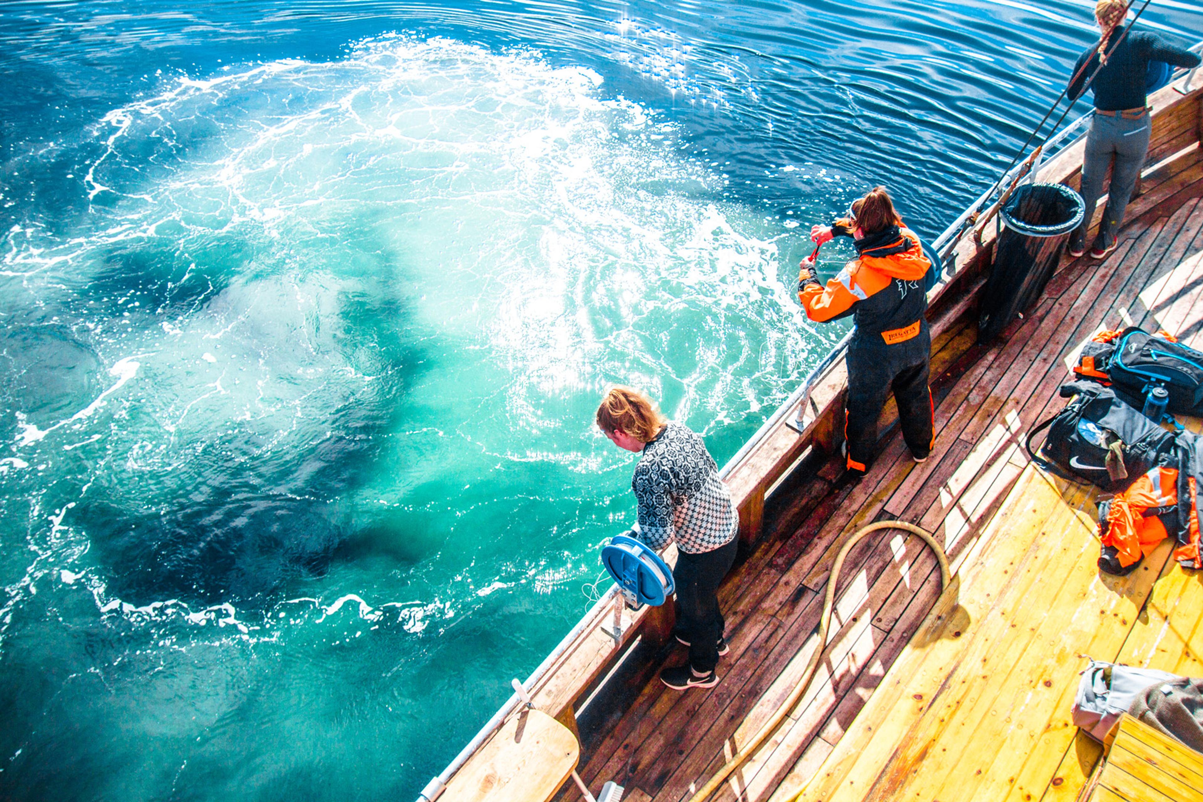 Two woman are looking for fish down into the sea from the boat