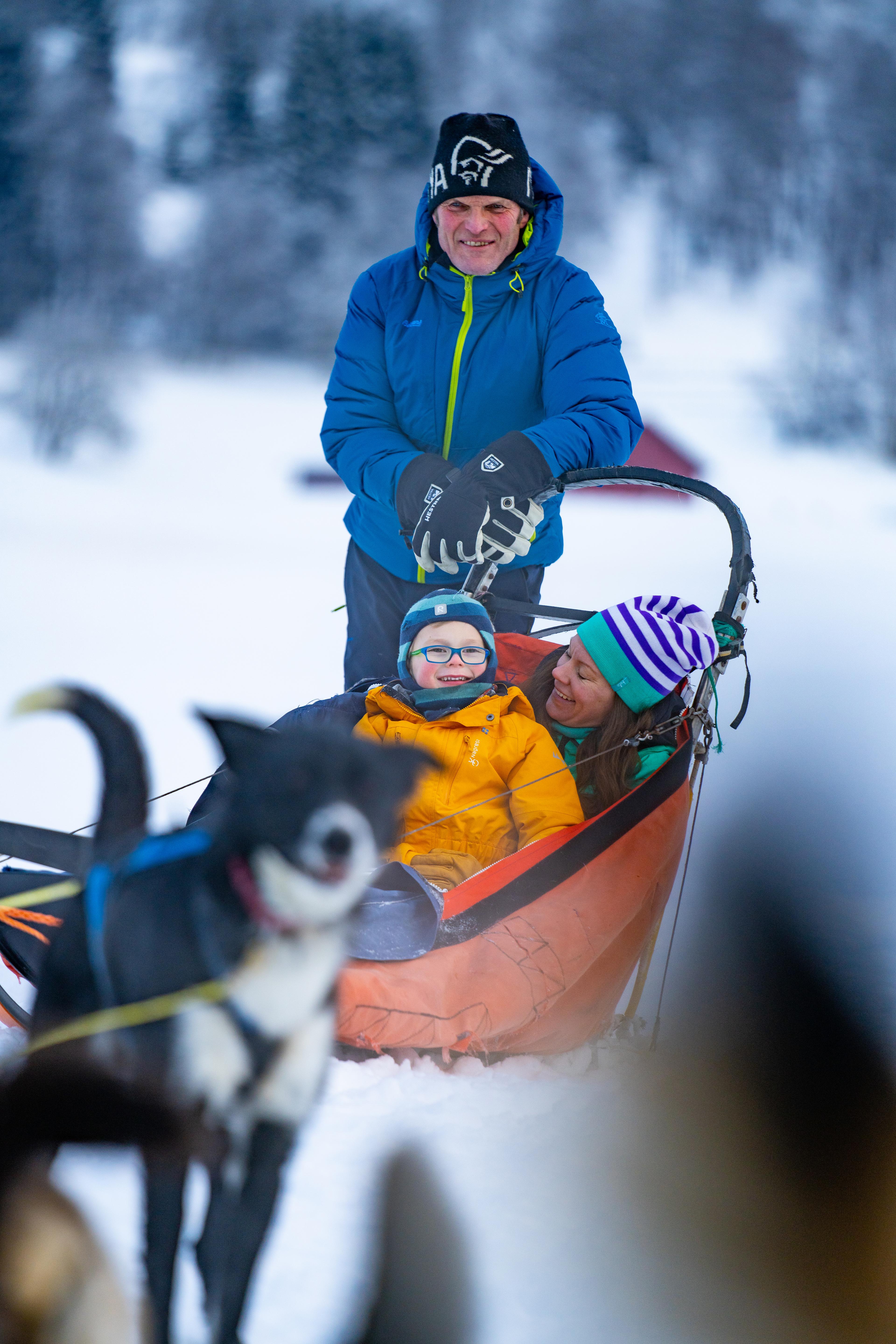 Familie på hundesledetur. Mor og barn sitter i sleden.