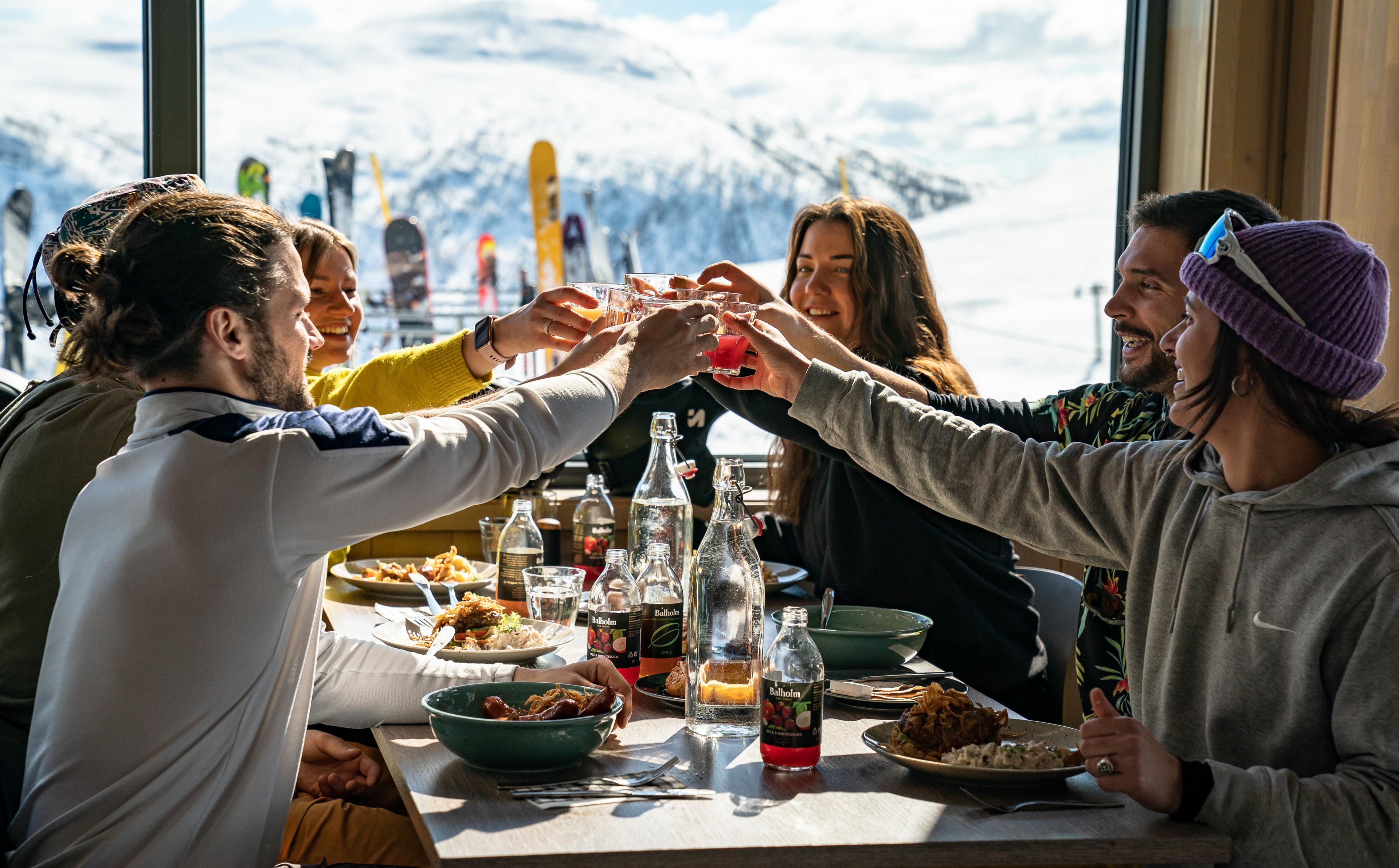 Venner i godt humør skåler og nyter et godt måltid på restaurant etter en dag på ski.
