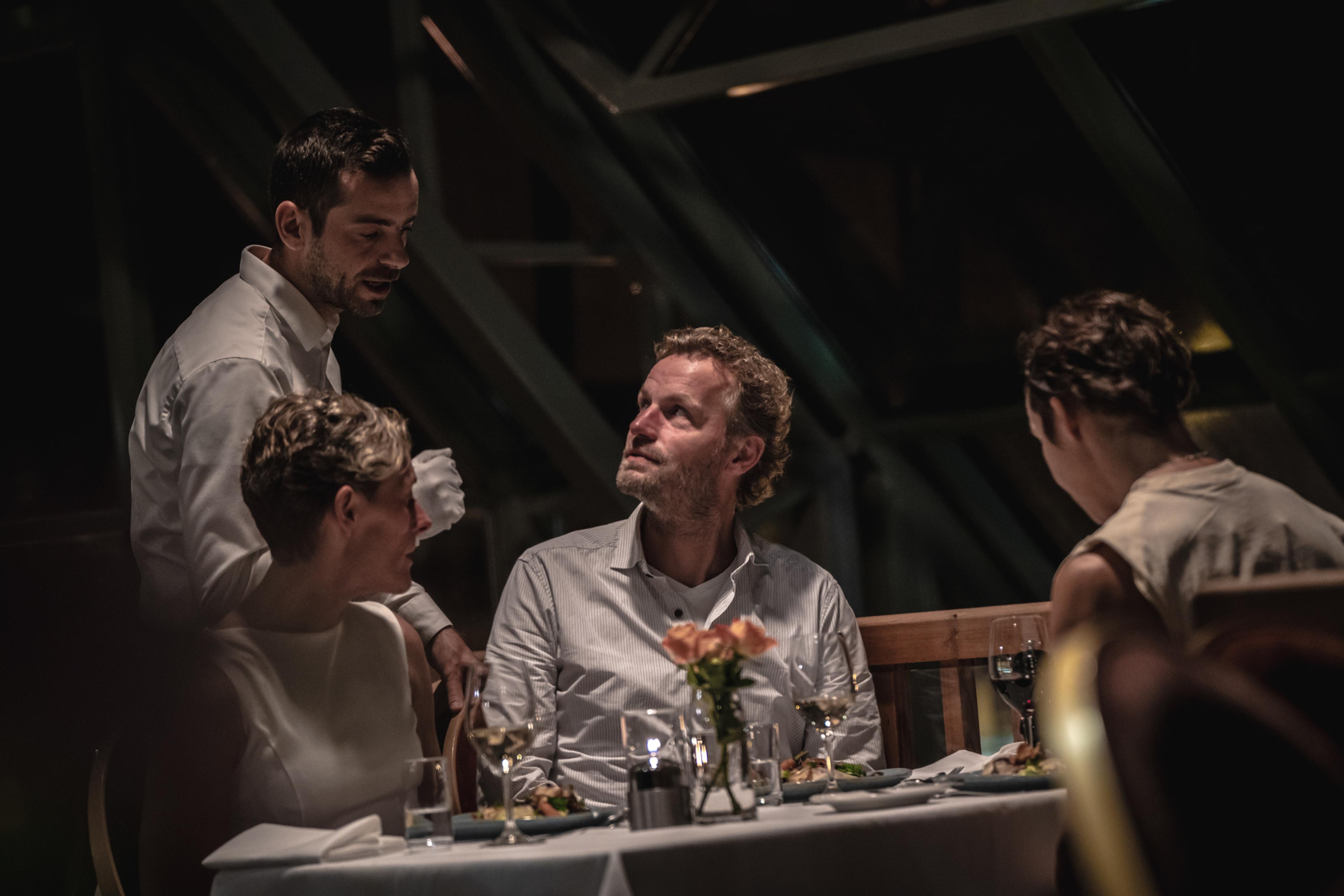 A waiter talks to customers at a table in restaurant Arven at Fretheim Hotel.