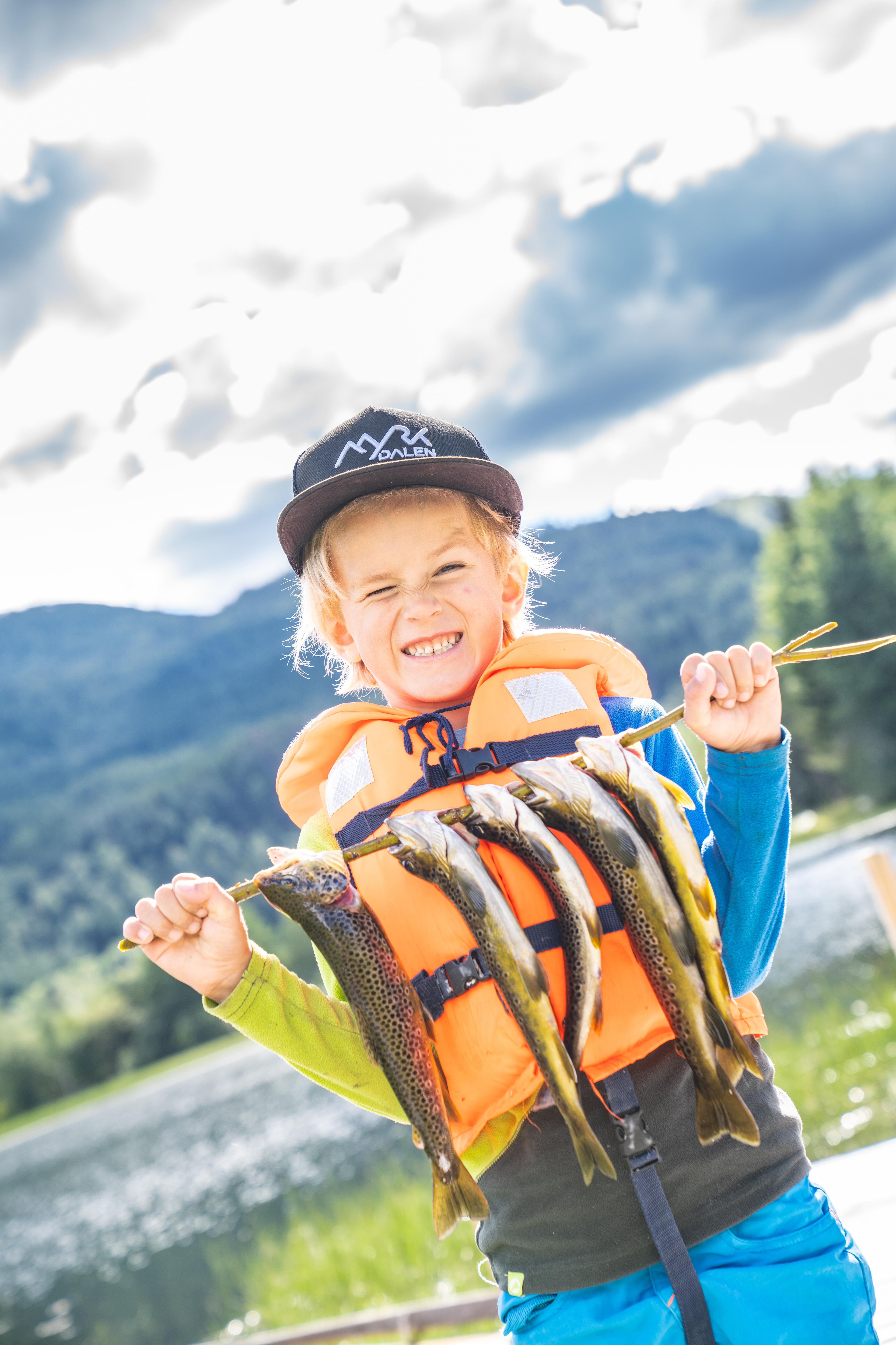 Happy boy shows off all the fish he has caught, which are now hanging in a row on a stick.
