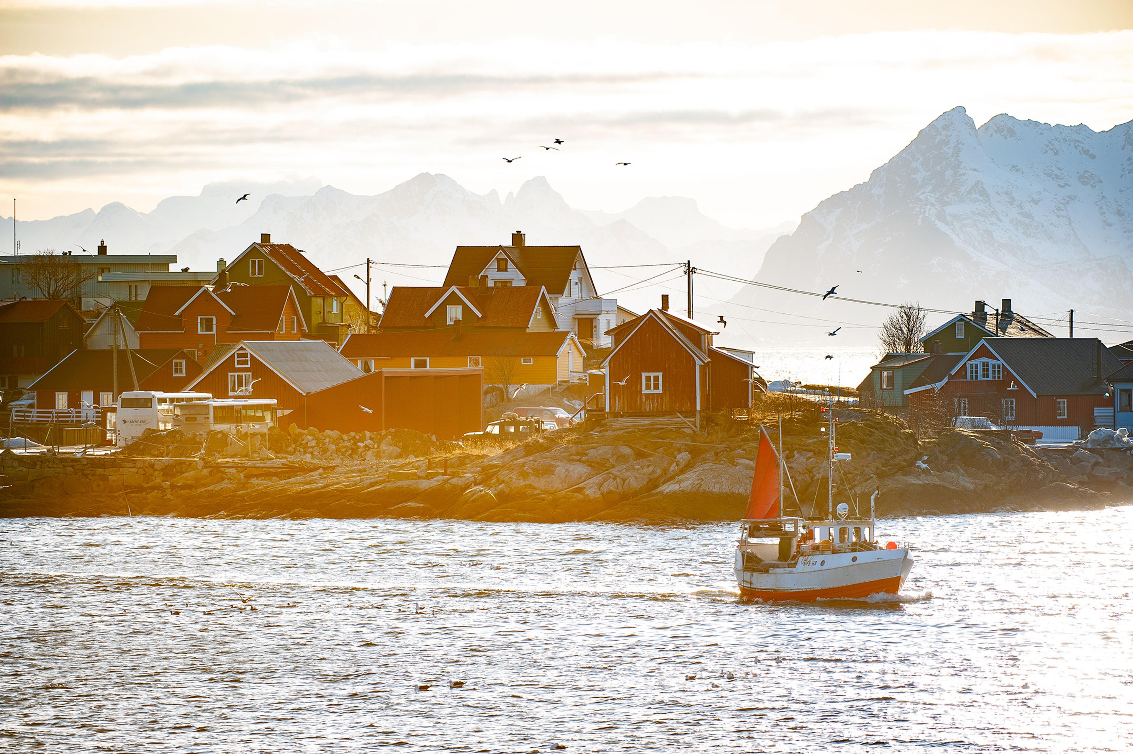  Un pequeño barco pesquero en el agua frente a Reine en Lofoten, montañas escarpadas con un poco de nieve detrás.