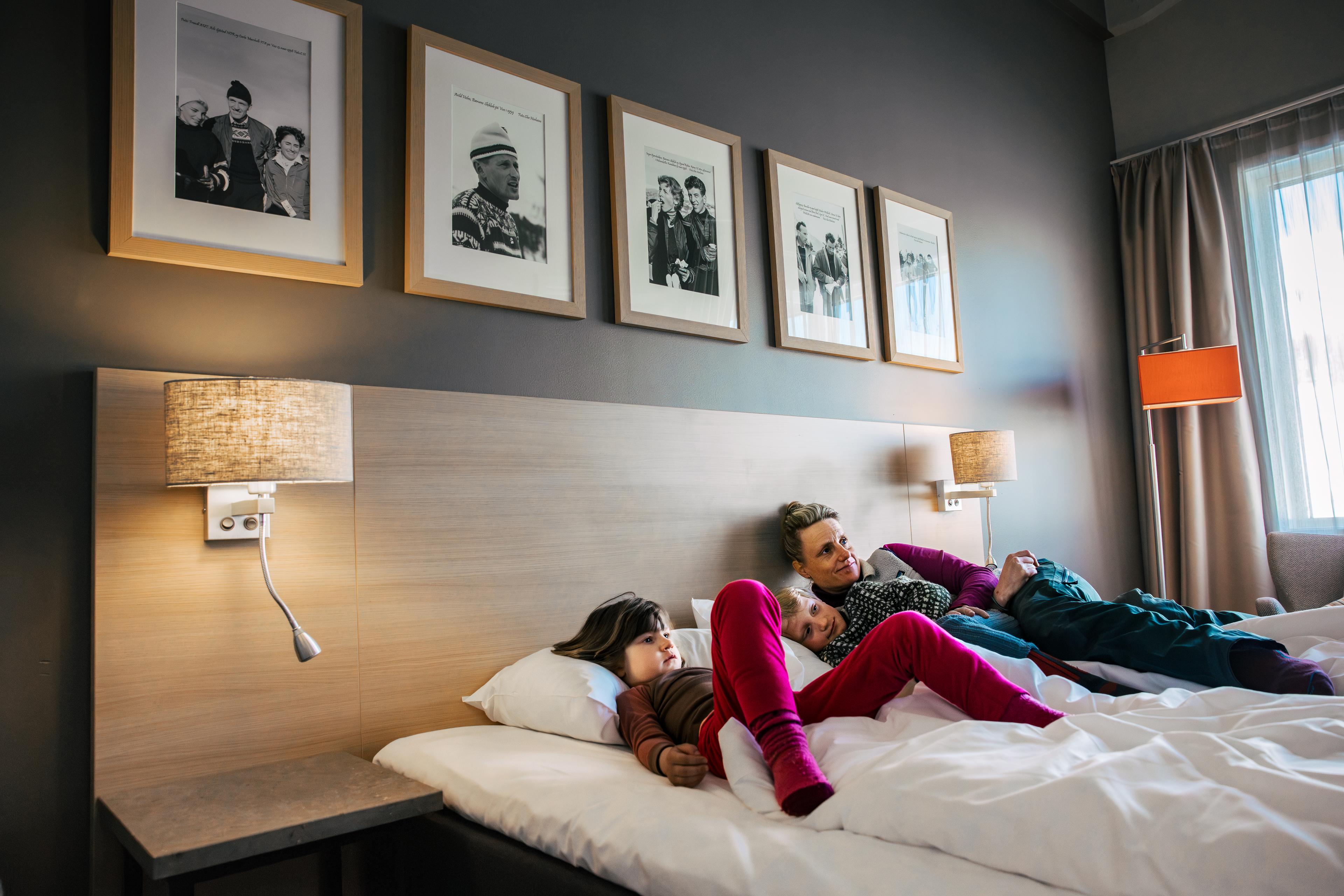 Mother and two children relax and watch TV in the hotel bed.