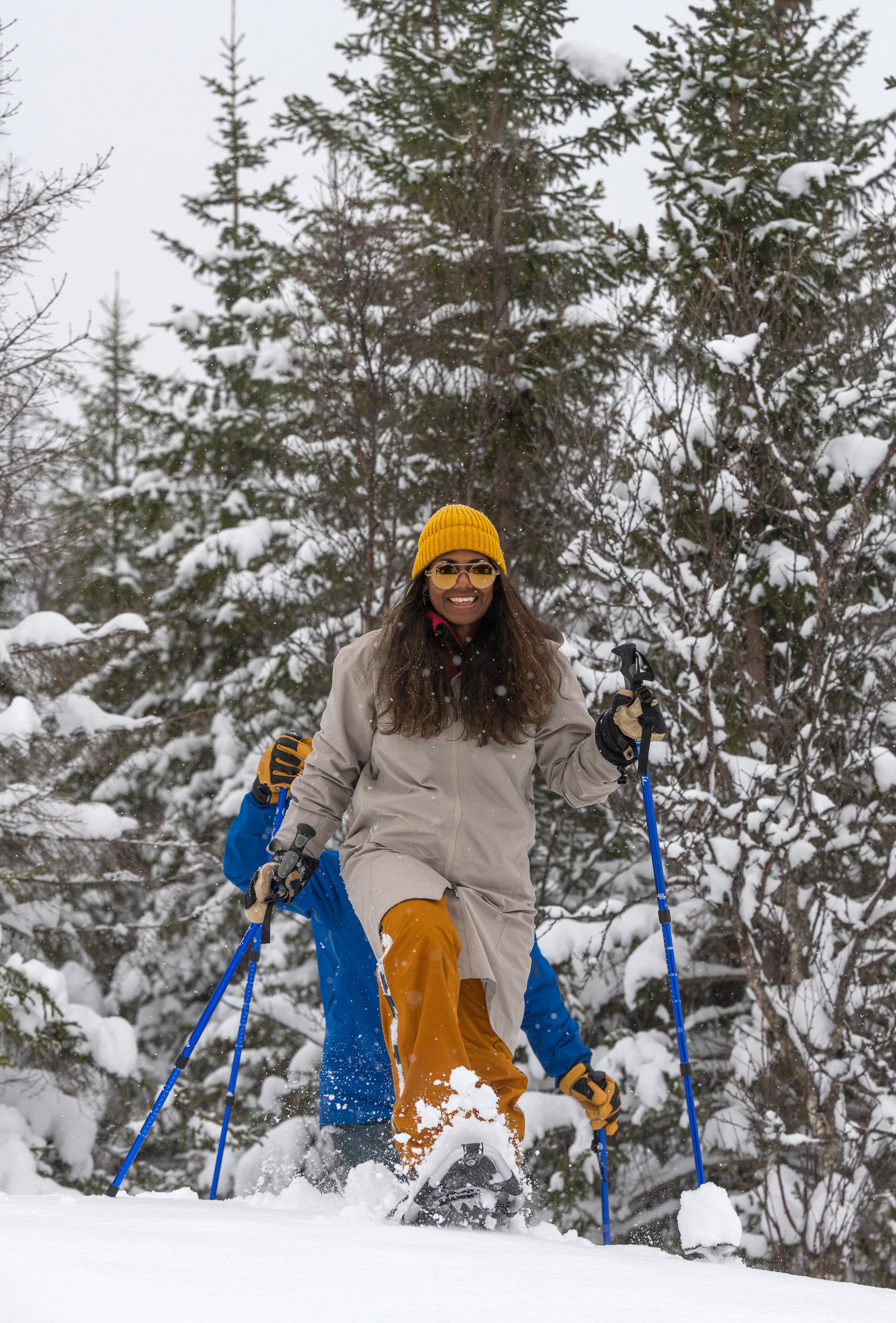 Woman wearing a yellow hat snowshoeing through a snow-covered forest.