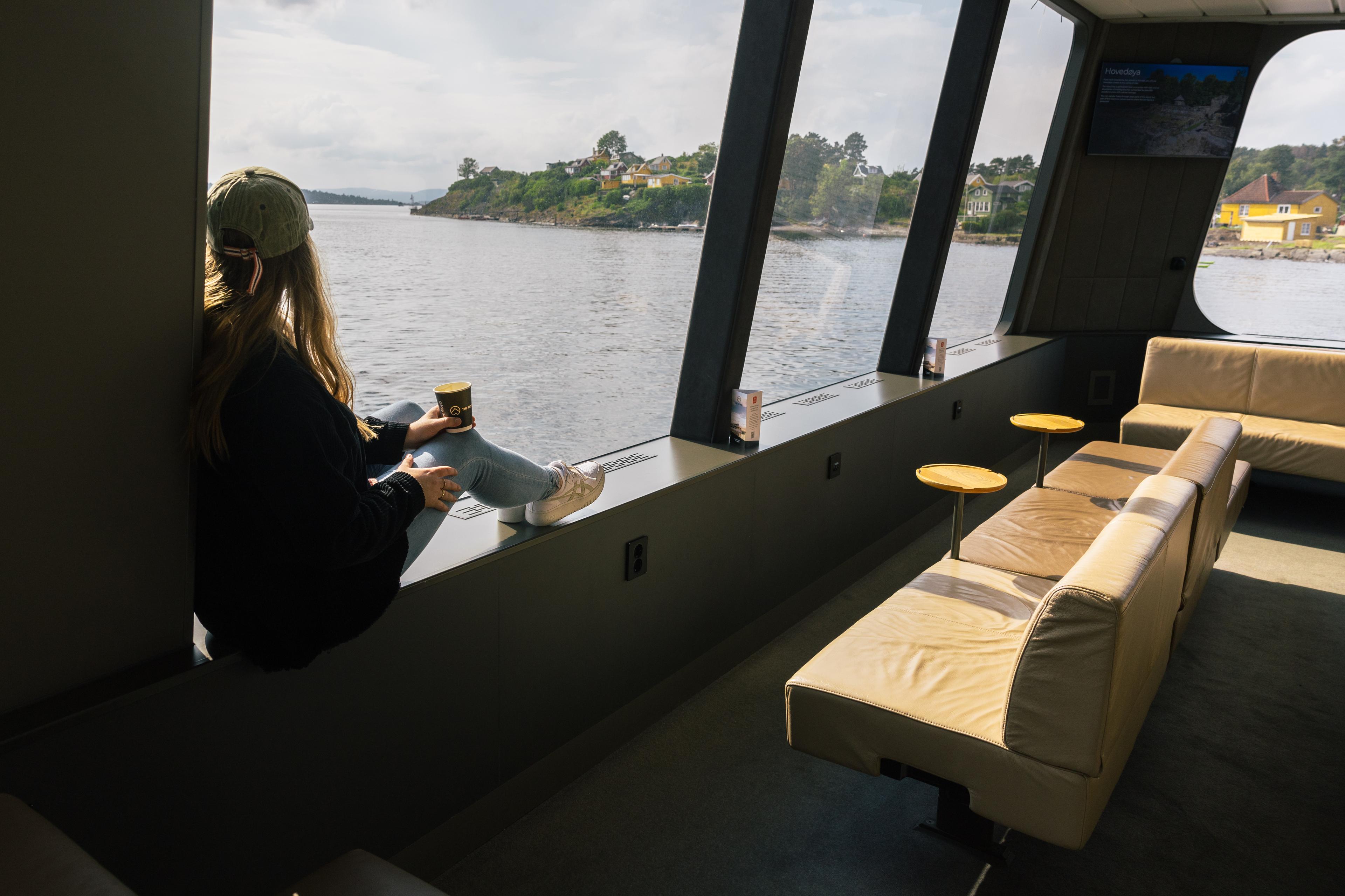 A woman sits on the windowsill of Vision of The Fjord looking out over the Oslofjord.