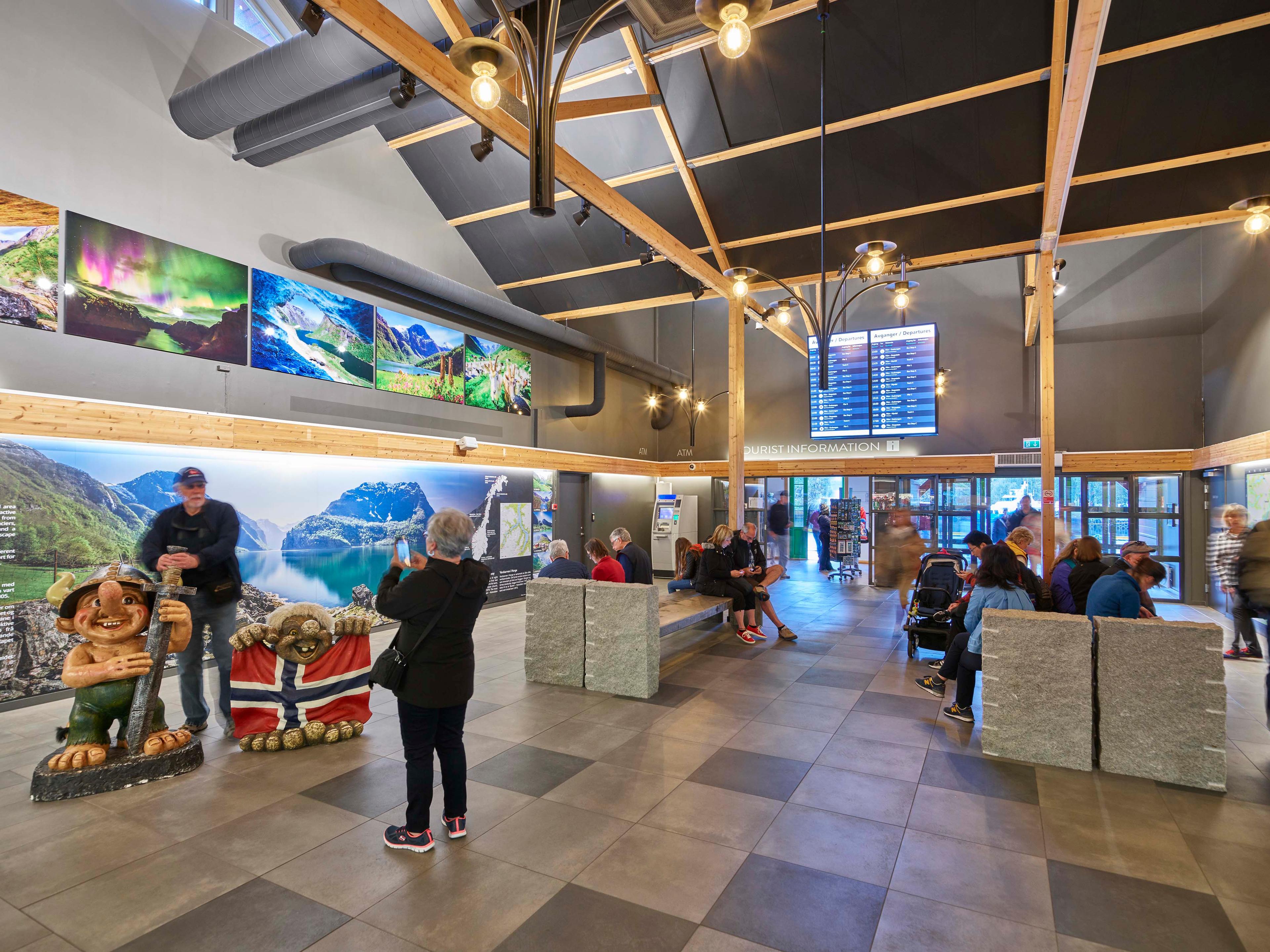 Ein Paar macht Fotos mit einer Trollfigur im Wartebereich des Flam Visitor Centers. Weitere Leute warten im Hintergrund.