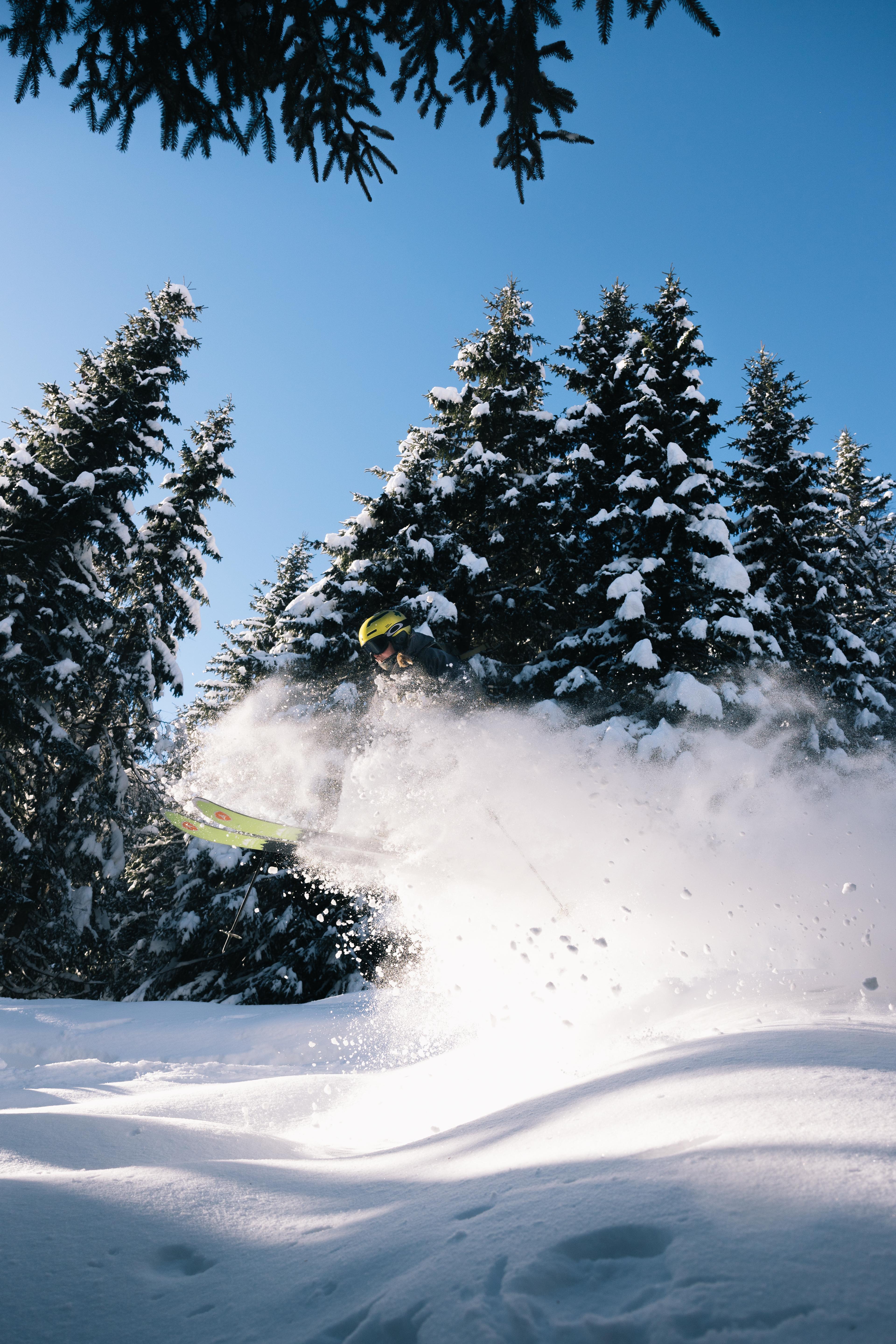 Skier skis down a jump in the forest so the snow is falling.