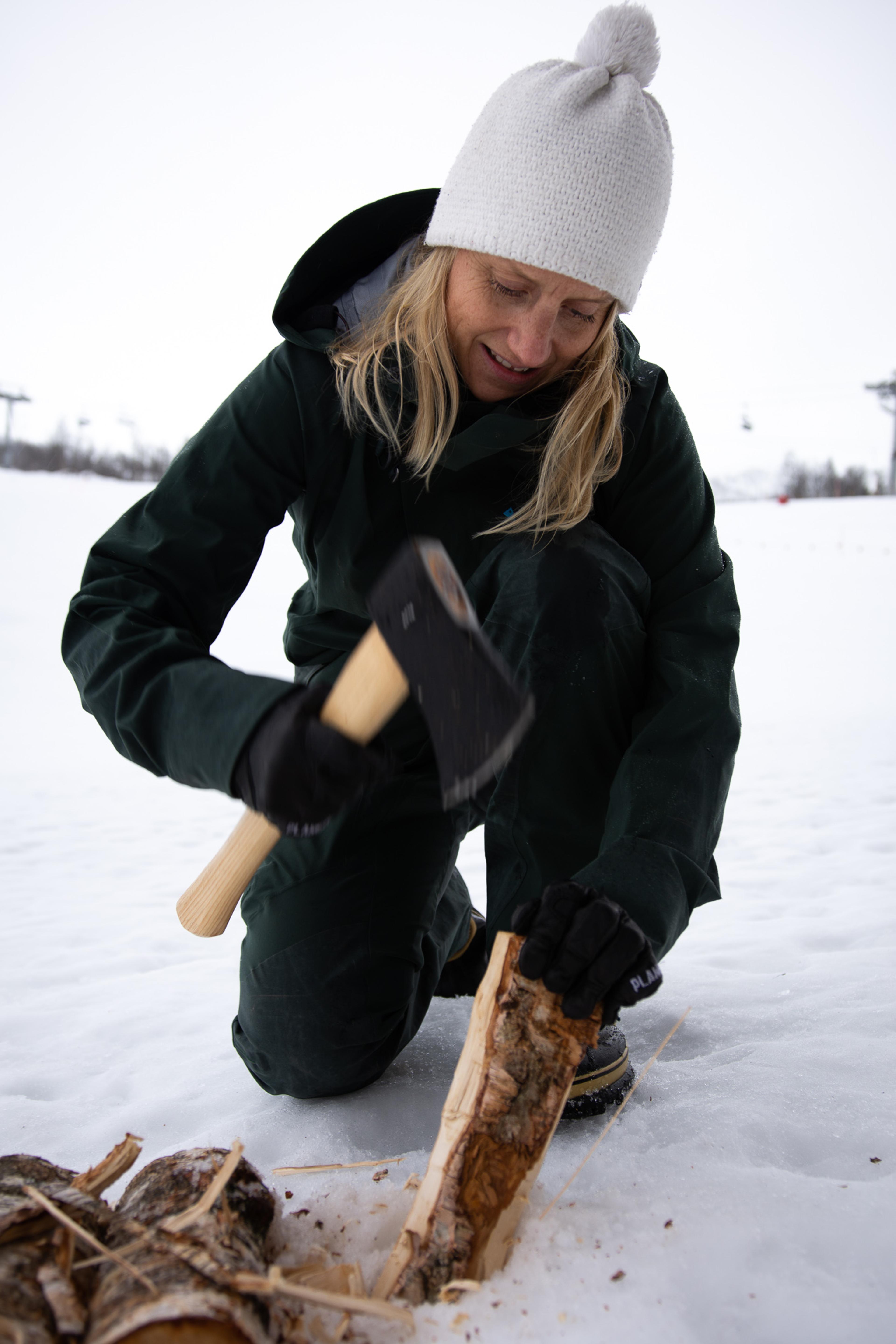 En kvinne hogger til vedkubber med øks for å lage bål i snøen.