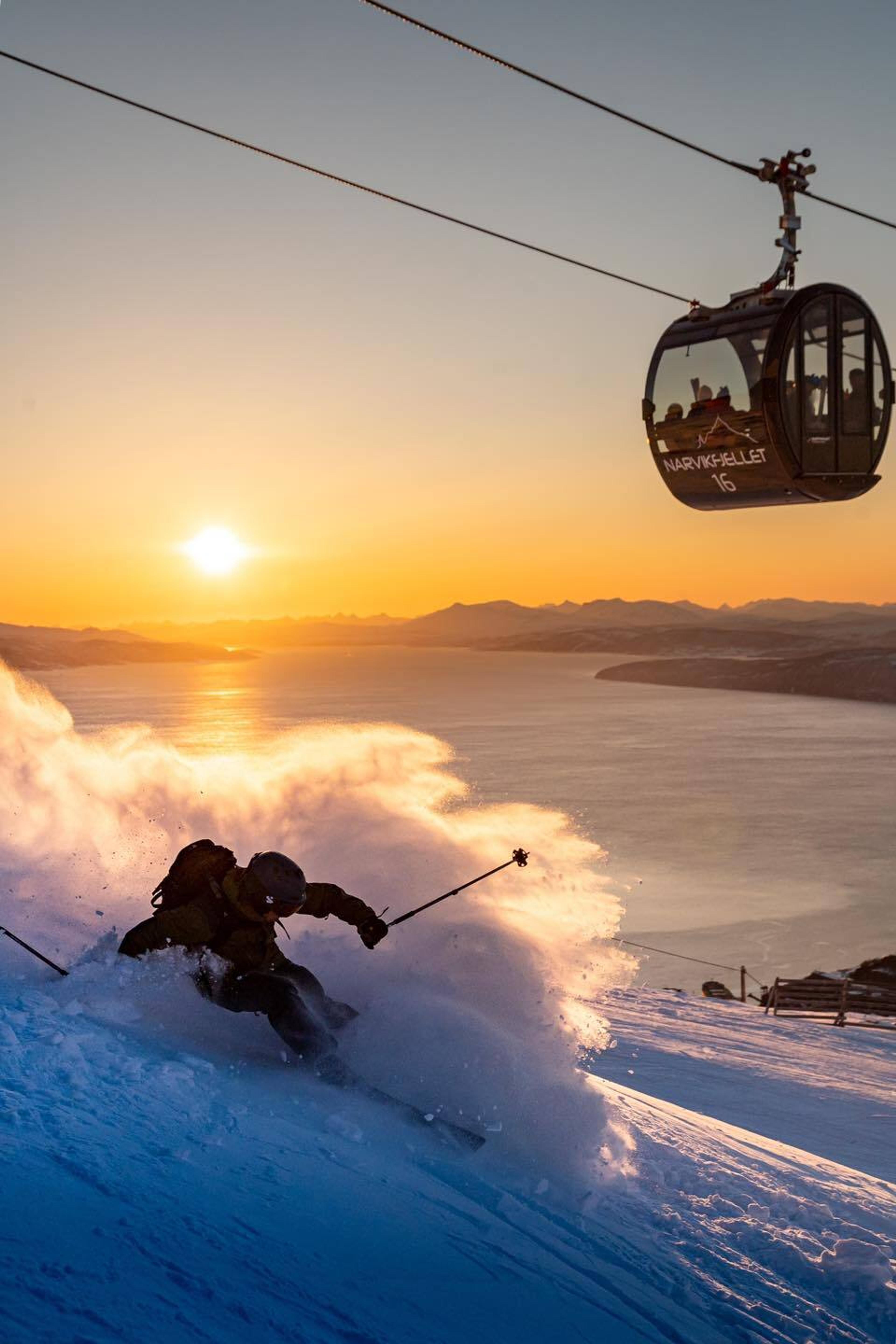 En mann står pudder under Narvik Gondol i lavt vinterlys. 